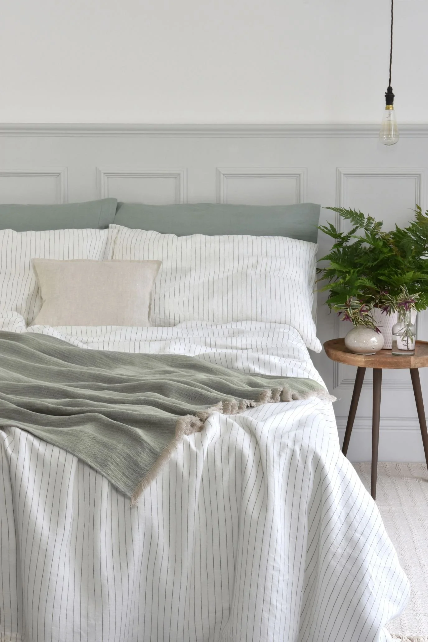 Bed styled with sage green linen bedding, white striped pillows and a loosely draped green throw.