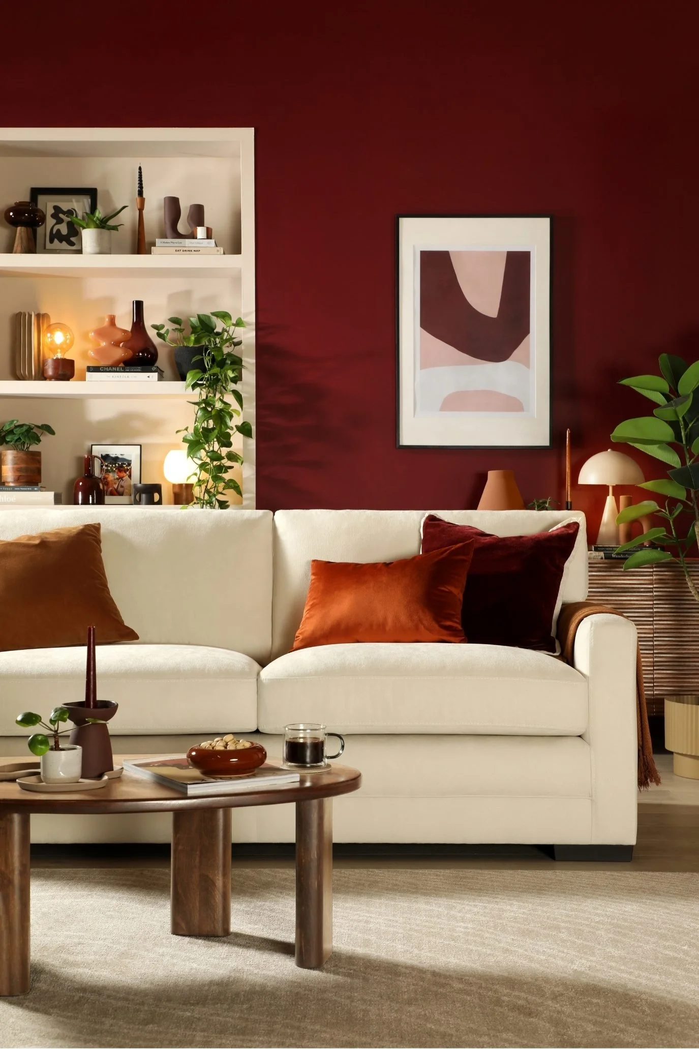 Rich red living room with off-white sofa, burgundy and brown cushions, natural wood and styled shelving.
