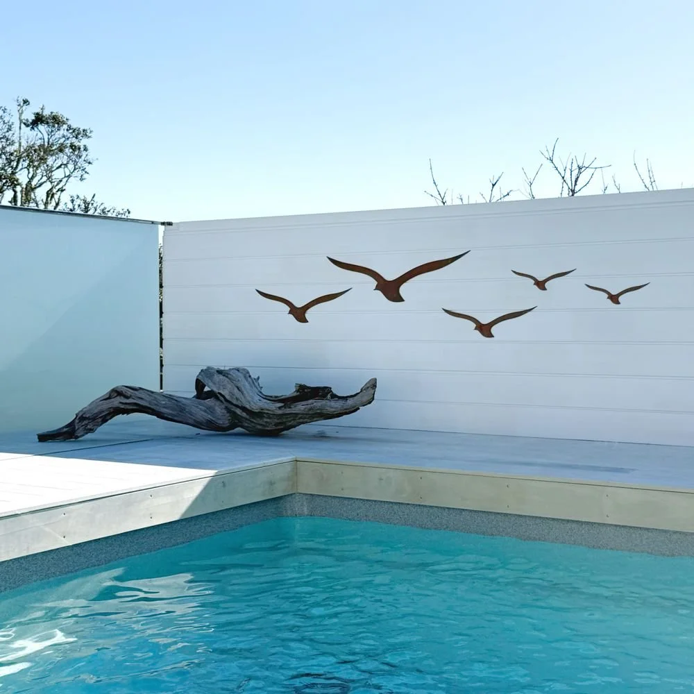 five bird sculptures on a white wall next to a swimming pool and wood sculpture