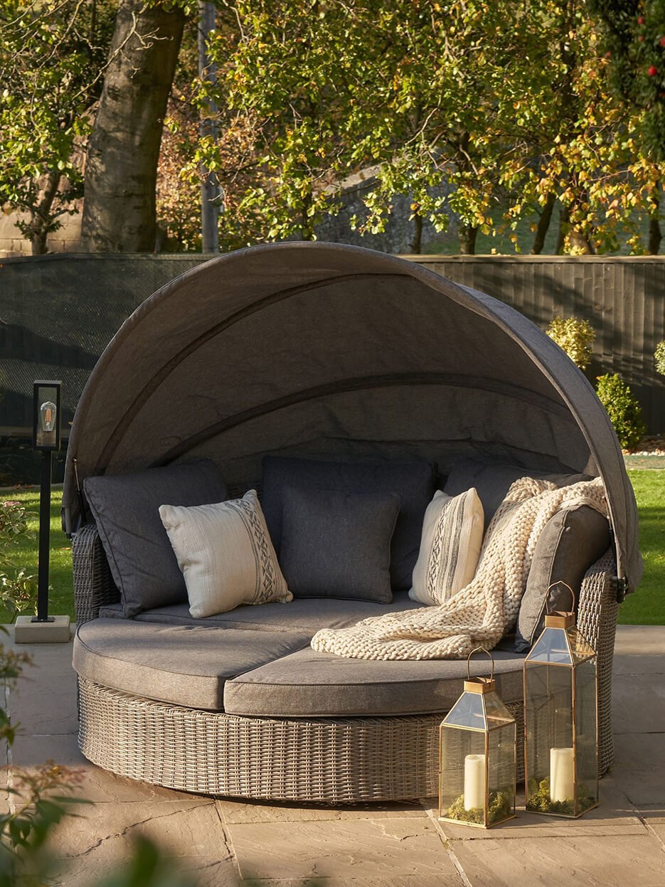 A circular day bed in dark grey with synthetic woven rattan and a large canopy