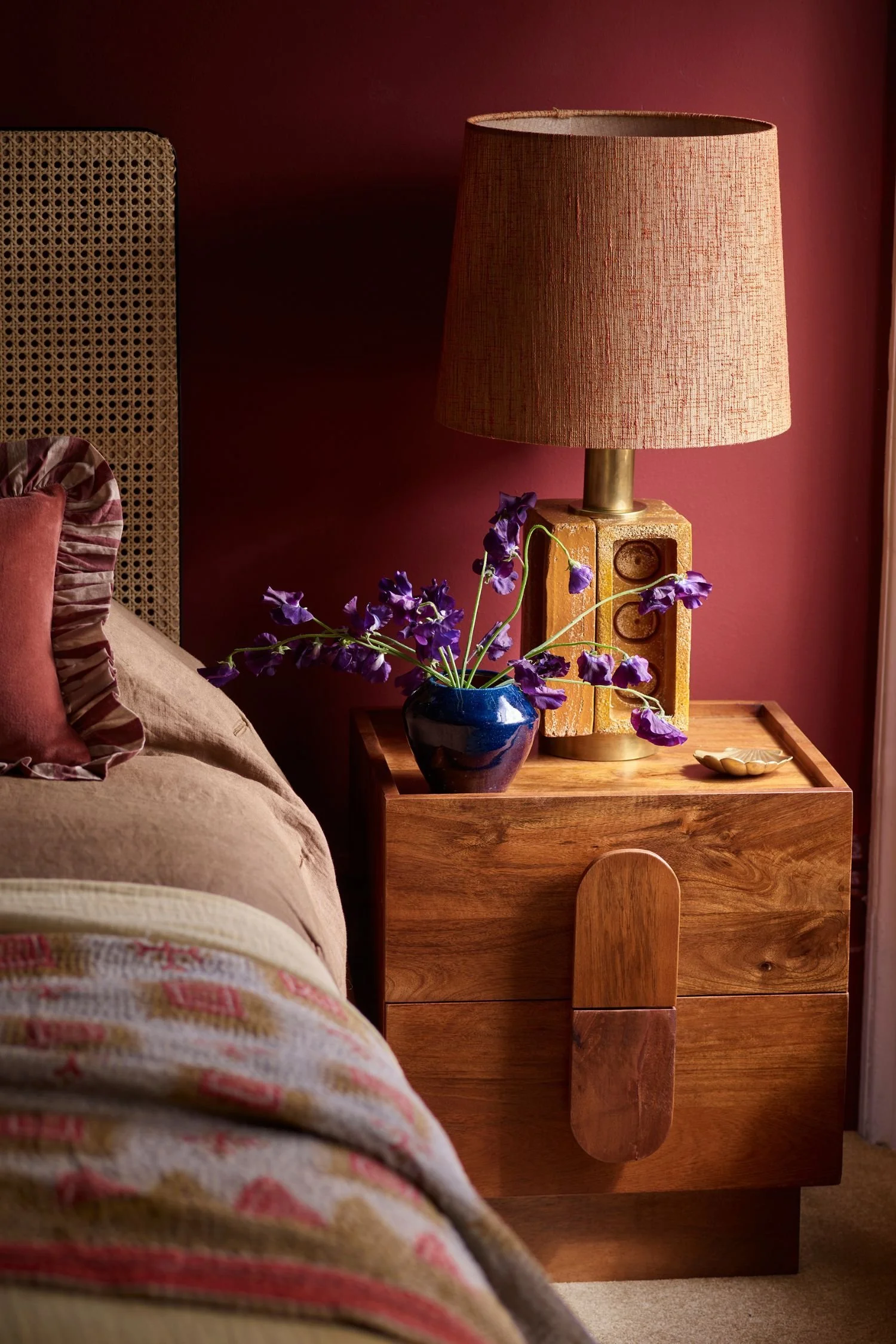 Warm wood nightstand with oversized curved handles against an earthy red bedroom wall