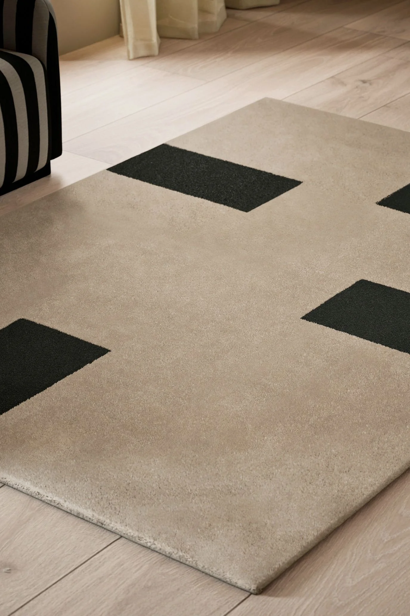 Kelly Hoppen x M&S beige rug with bold black geometric detailing on a pale wooden floor.
