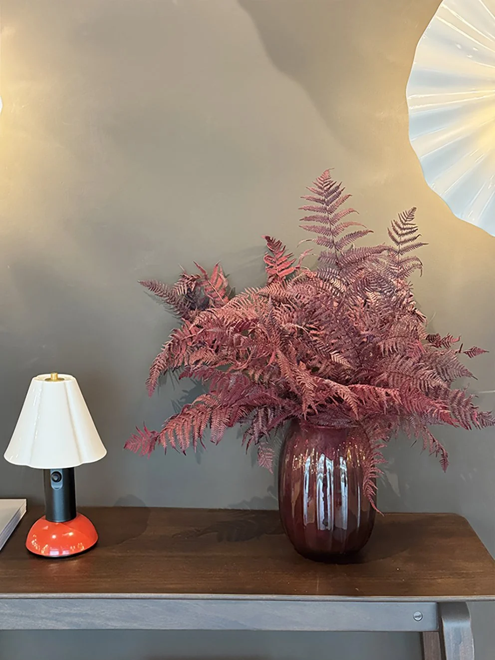 Dried pink-dyed fern leaves in a pink vase on a table next to a lamp