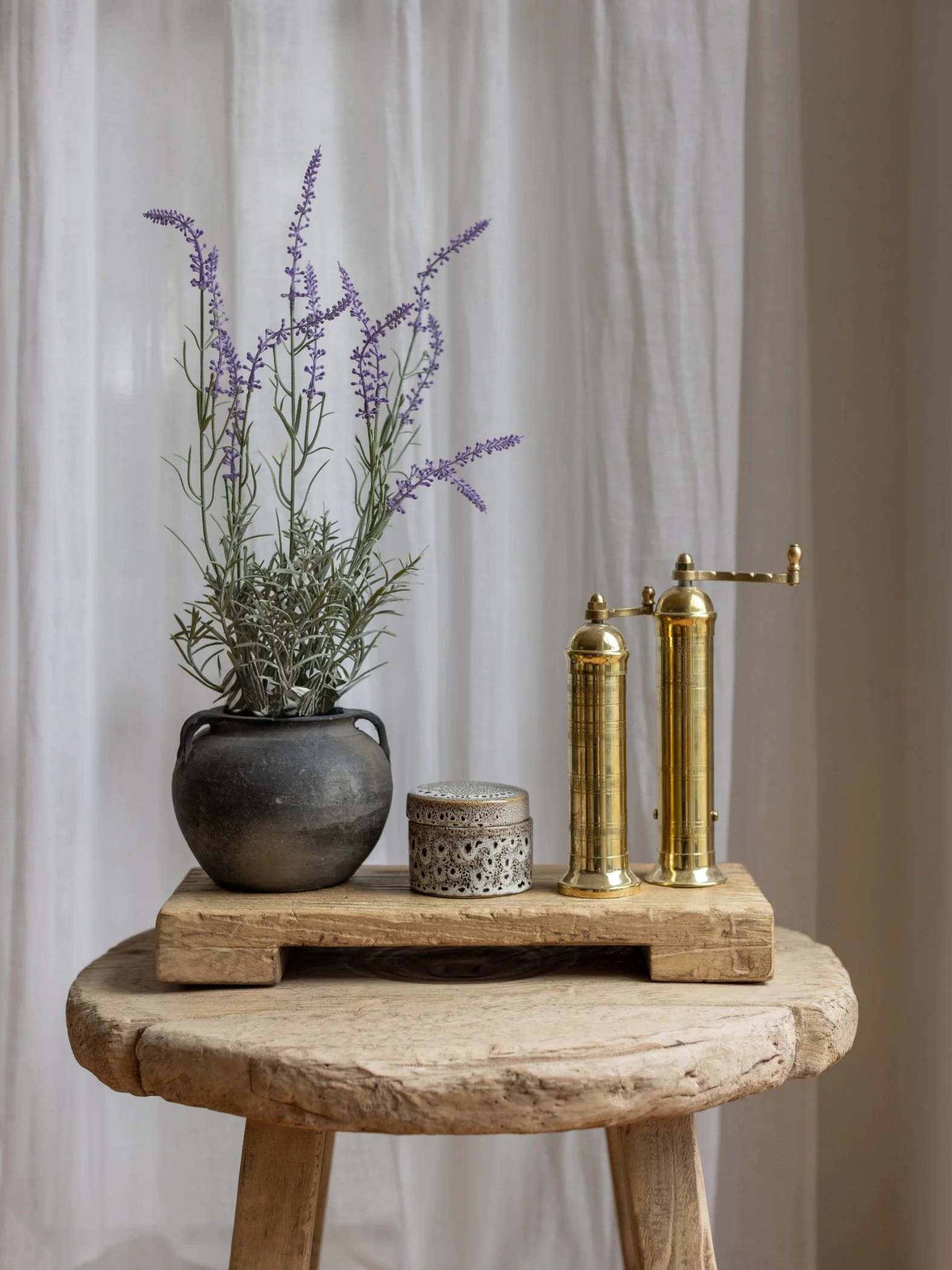 A wooden riser with brass salt and pepper grinders next to a trinket box and pot with lavender.