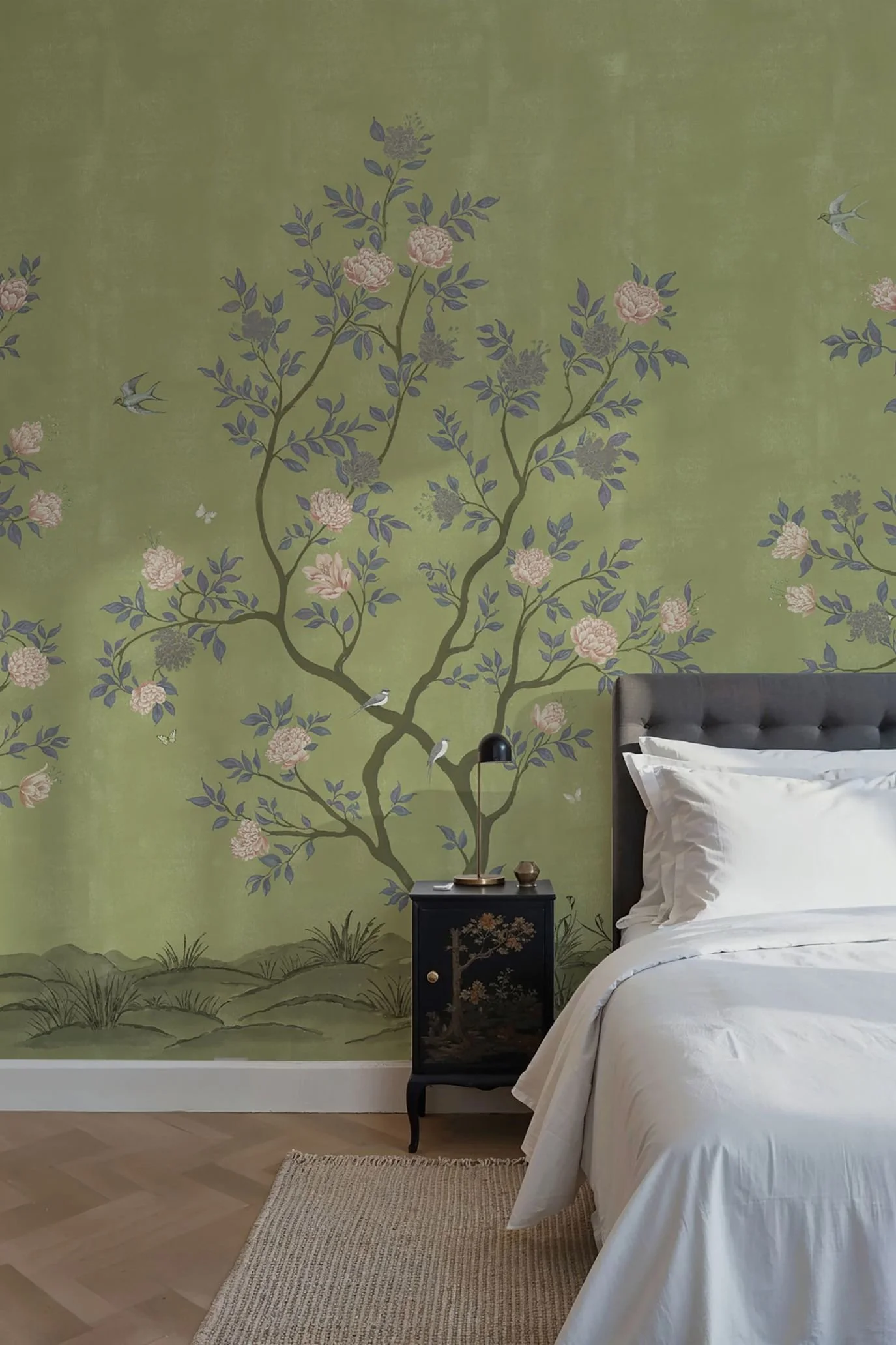 Soft green chinoiserie wallpaper with flowering branches behind a dark upholstered bed with white bedding.