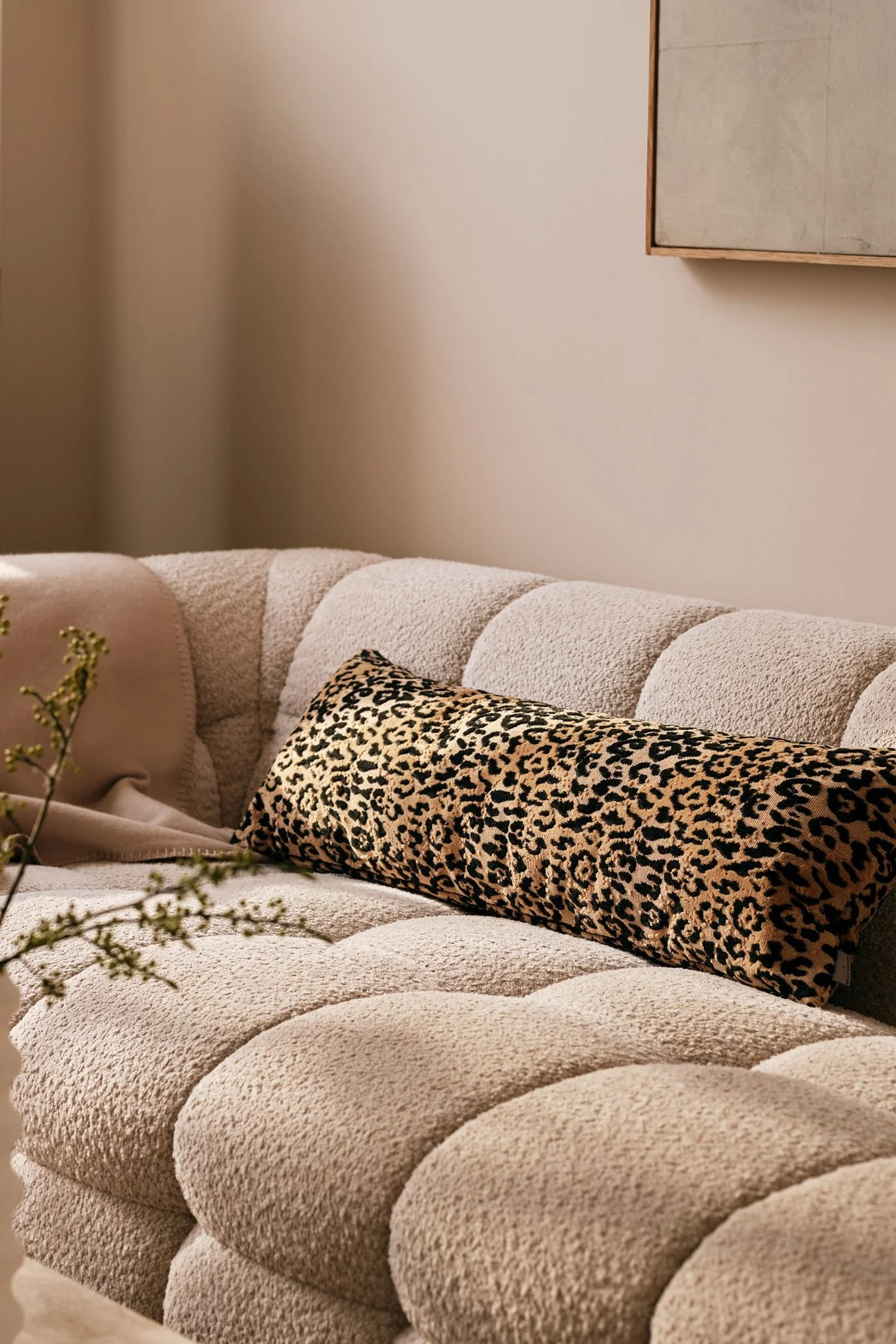 Kelly Hoppen x M&S leopard-print rectangular cushion on a cream textured sofa beside flowering branches.