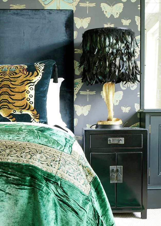 black oriental style nightstand with a snake base and feather shade lamp next to a bed with an emerald green throw and tiger cushion