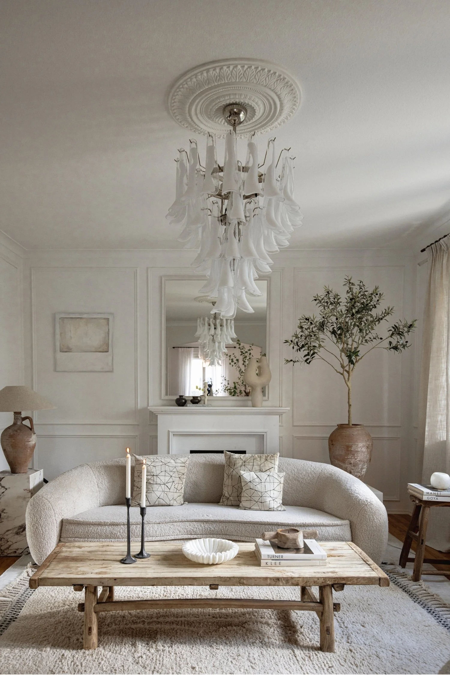 A room with an off-white sofa, with off-white walls a wooden coffee table and tall plant