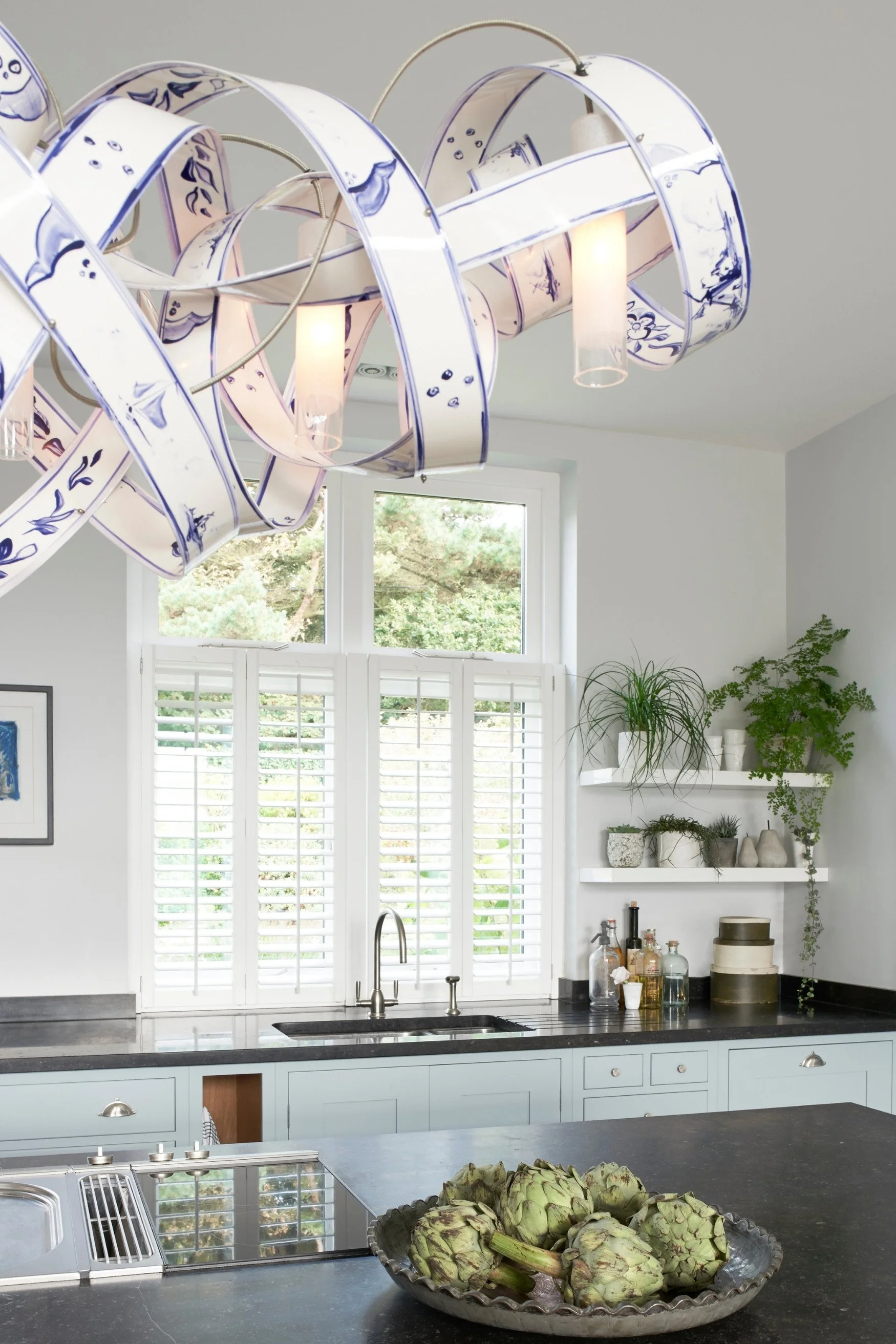 A sculptural light with Delft Blue pattern above a grey worktop with a pale blue kitchen behind