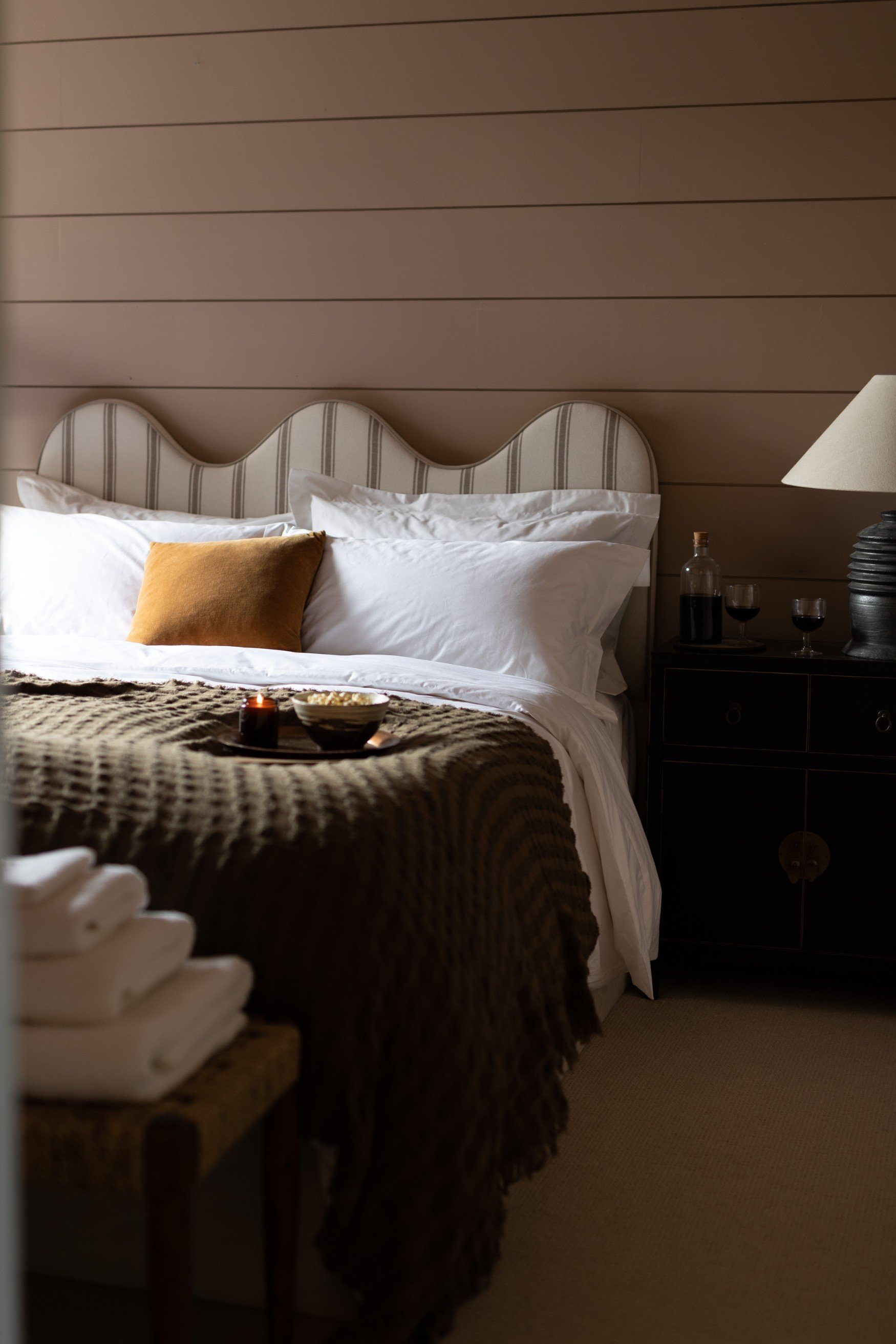 Wavy shaped stripy head board with white pillows and a yellow cushion and a brown waffle throw