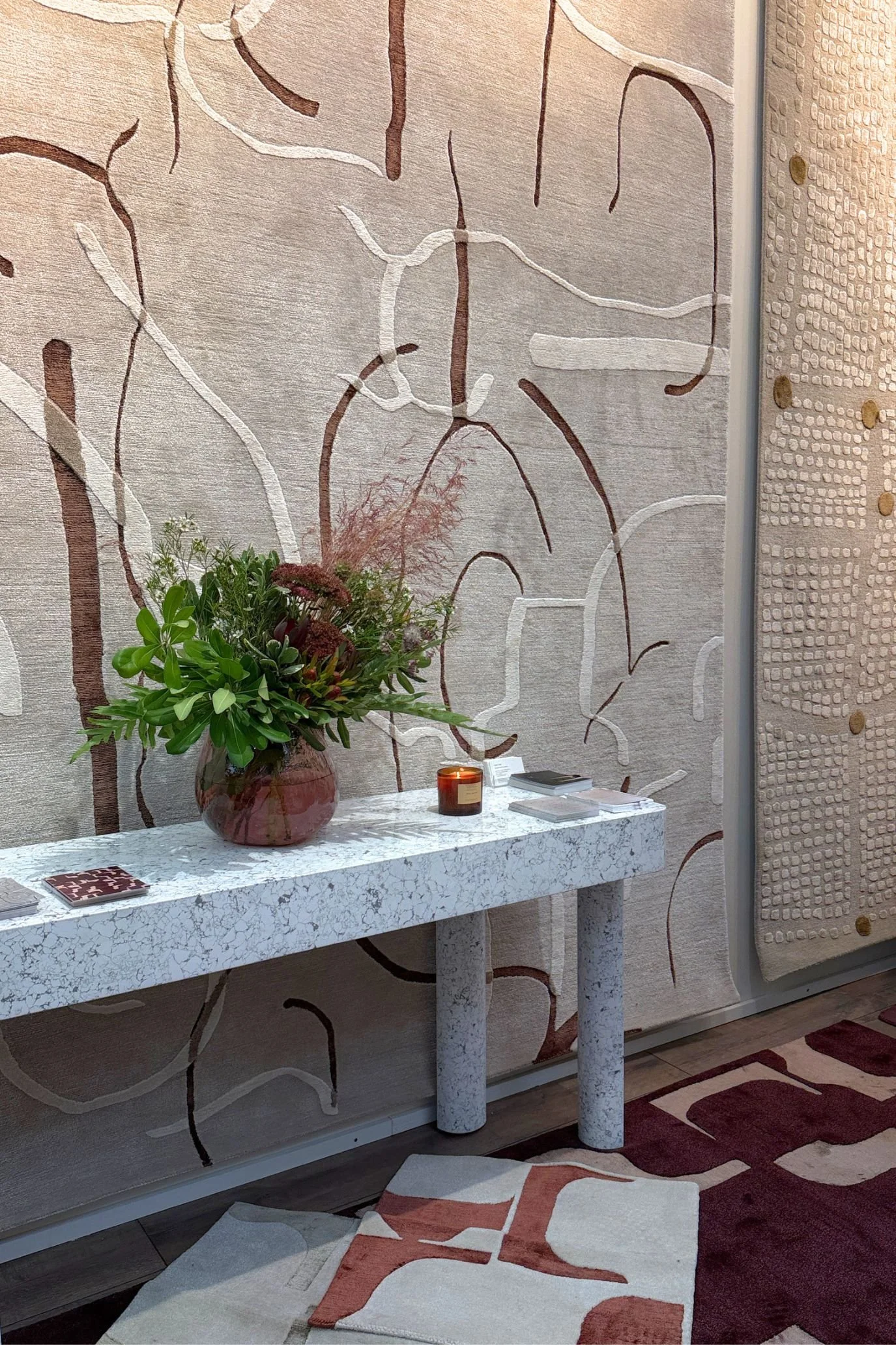 Large abstract rug displayed on a wall behind a pale console, with another patterned rug underfoot.