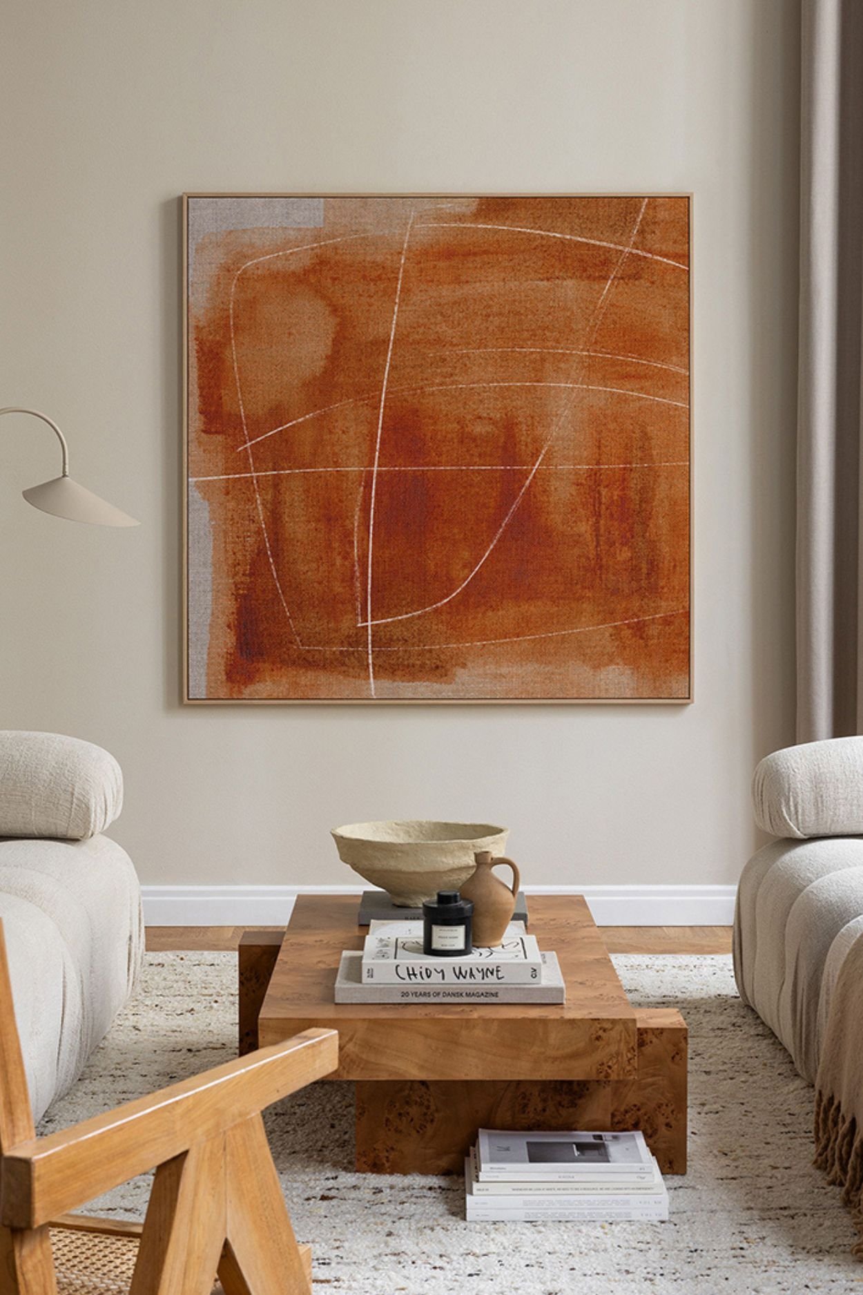 A living room with burnt orange abstract artwork on a beige wall with cream sofas either side