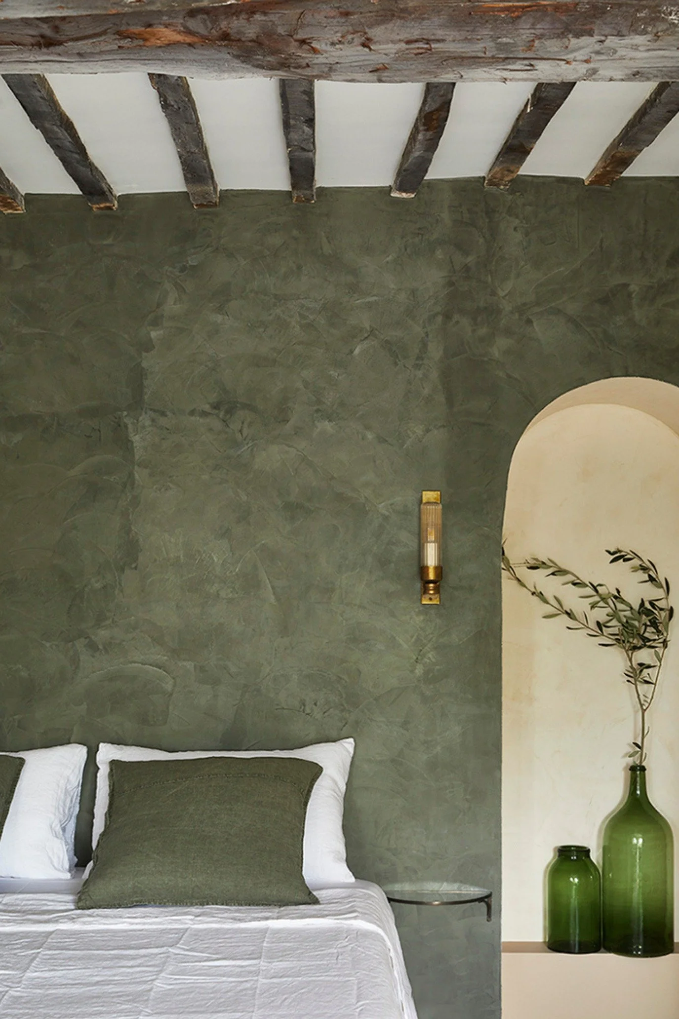 Elegant boutique hotel-style bedroom with textured green walls, limestone finishes, vintage furniture and layered green decor.