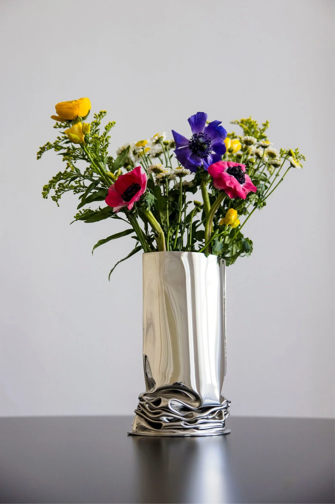 Sculptural metal Crash Vase with a deliberately crumpled base and fresh flowers.