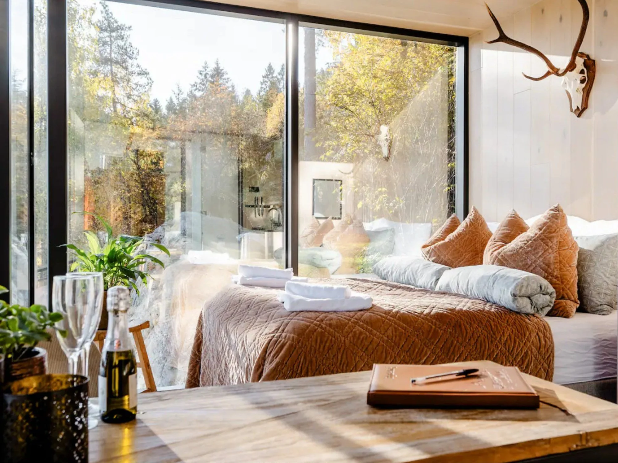 Scandinavian cabin bedroom with layered bedding, warm wood interiors and large windows overlooking snowy woodland.