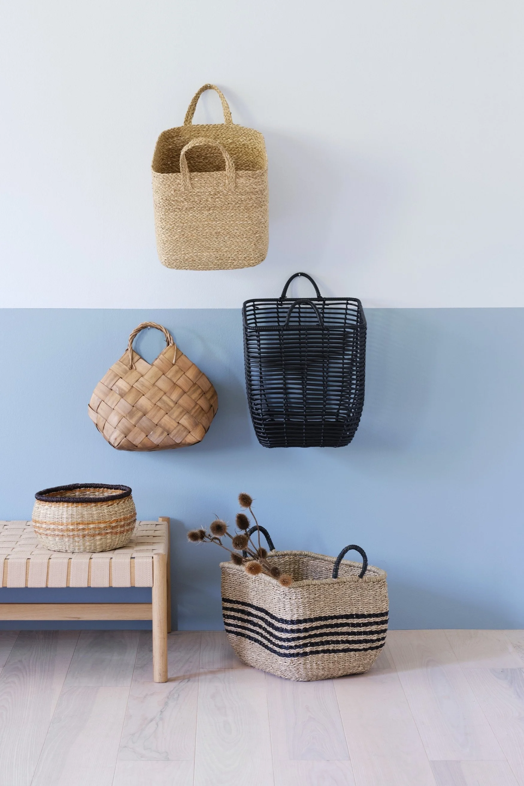 A wall painted in pale and a deeper blue with a selection of bags and baskets  hanging against the wall