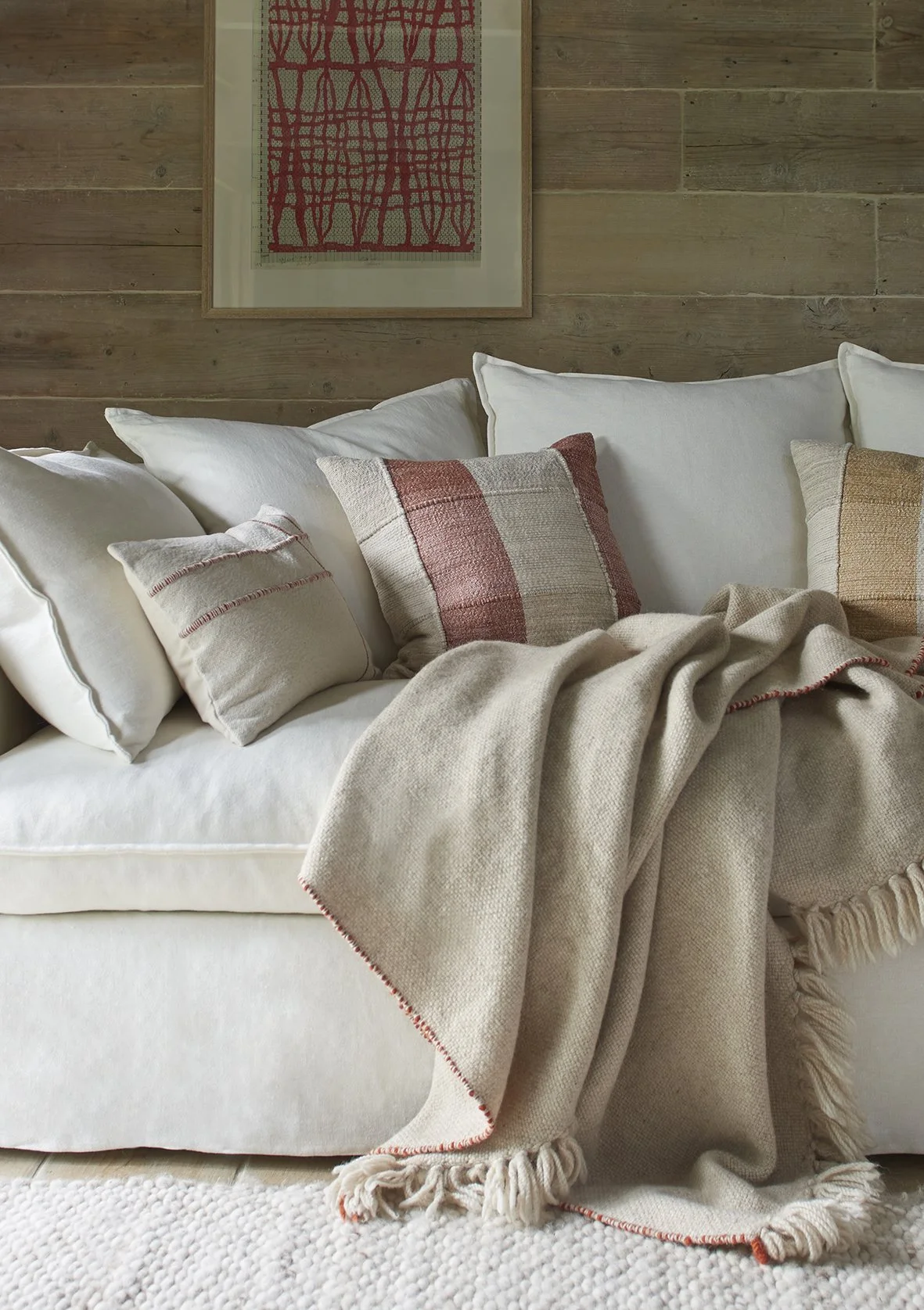 Home decor items stylish throw on a cream linen sofa with cushions in cream and earthy colours set against a rustic wood clad wall with a