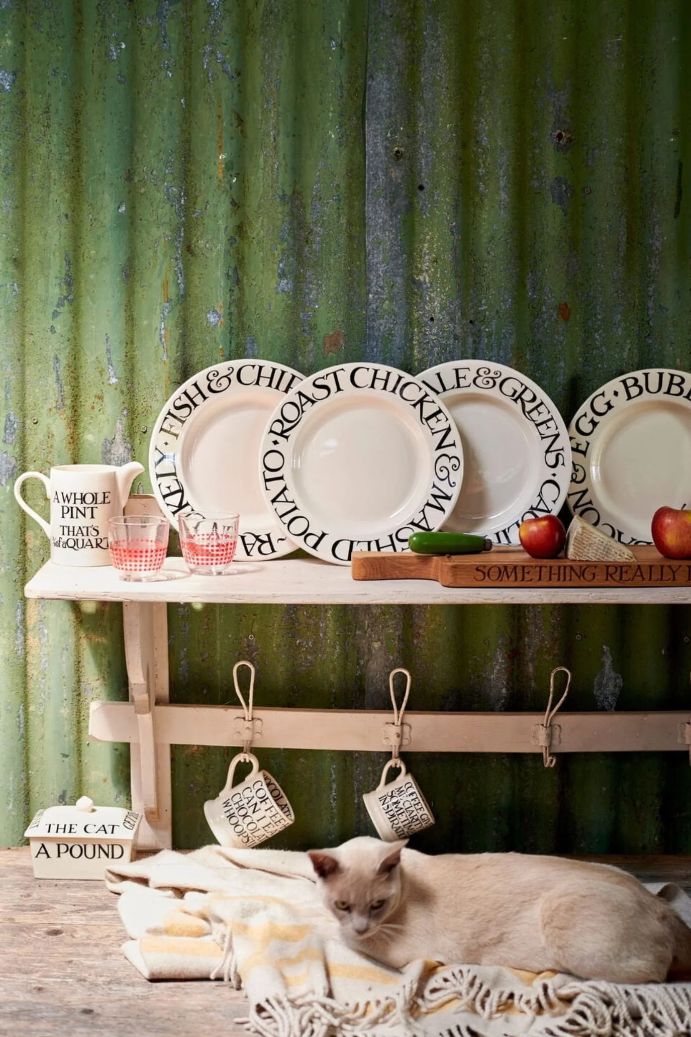 Plates with wording around rim displayed on a wooden shelf wrack next to a jug