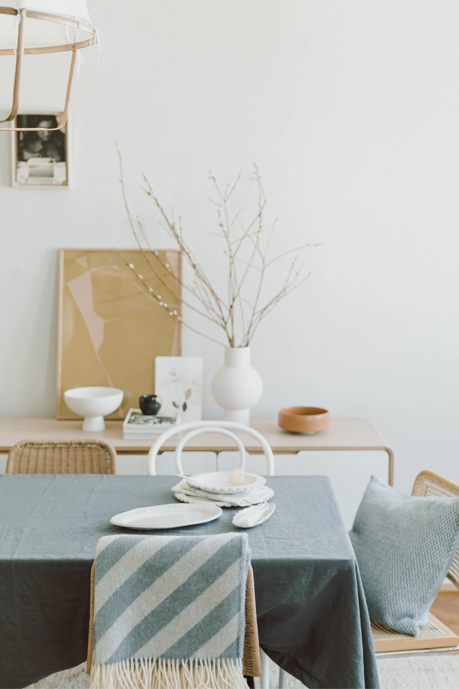 A dining area styled with a blue throw and various vessels behind the table displayed in white