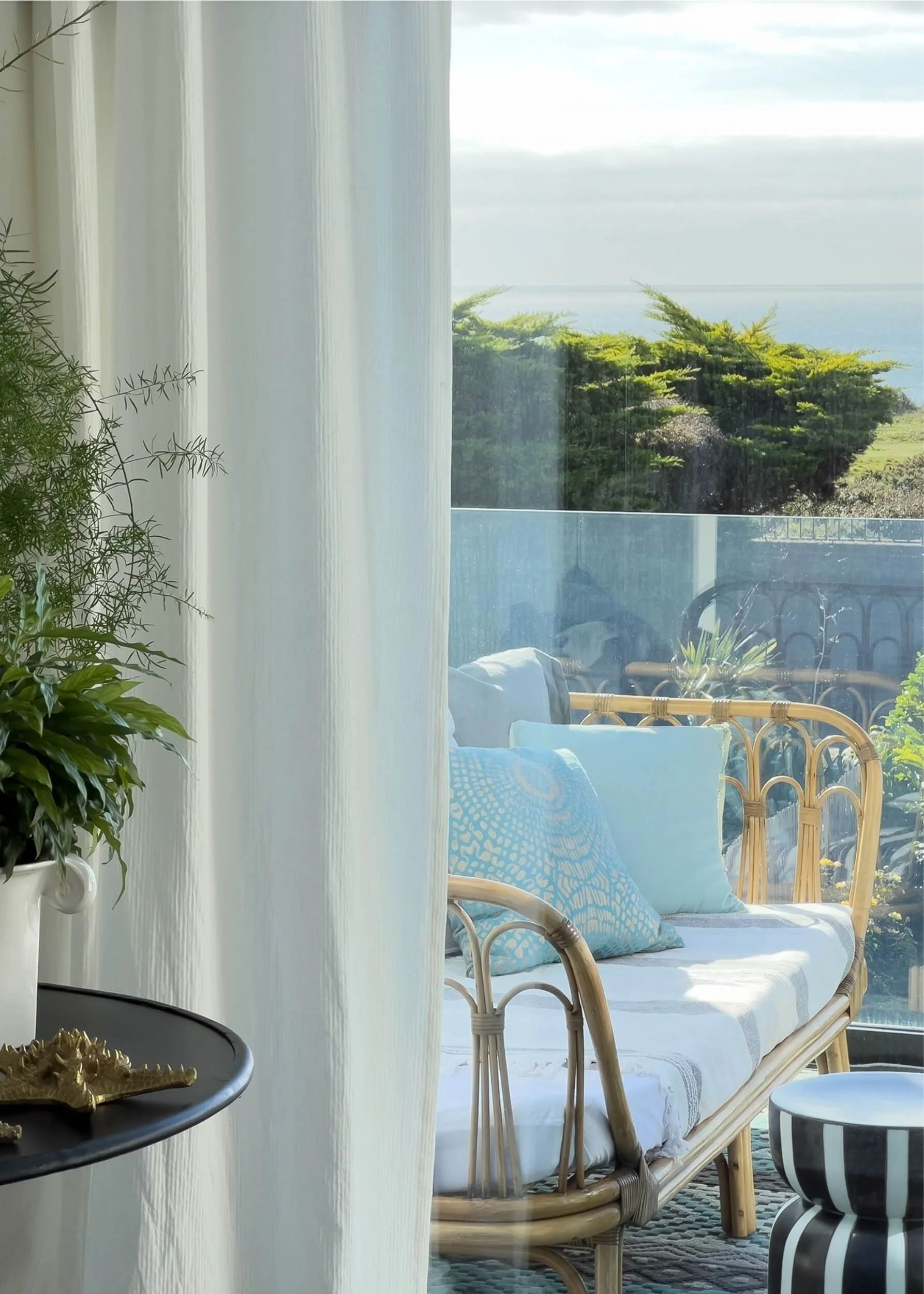 a balcony overlooking the sea with a bamboo day bed styled with aqua toned cushions.