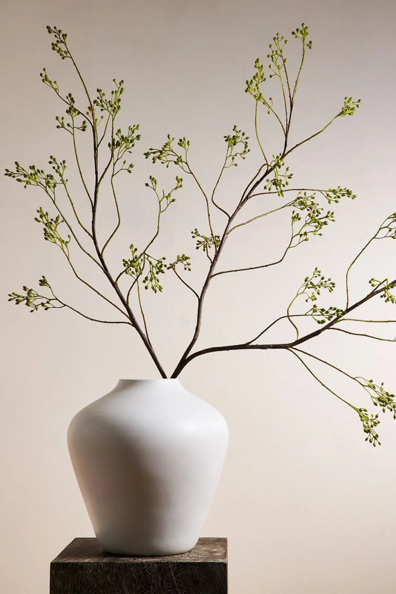 Tall faux green flowering branches displayed in a simple white vase.