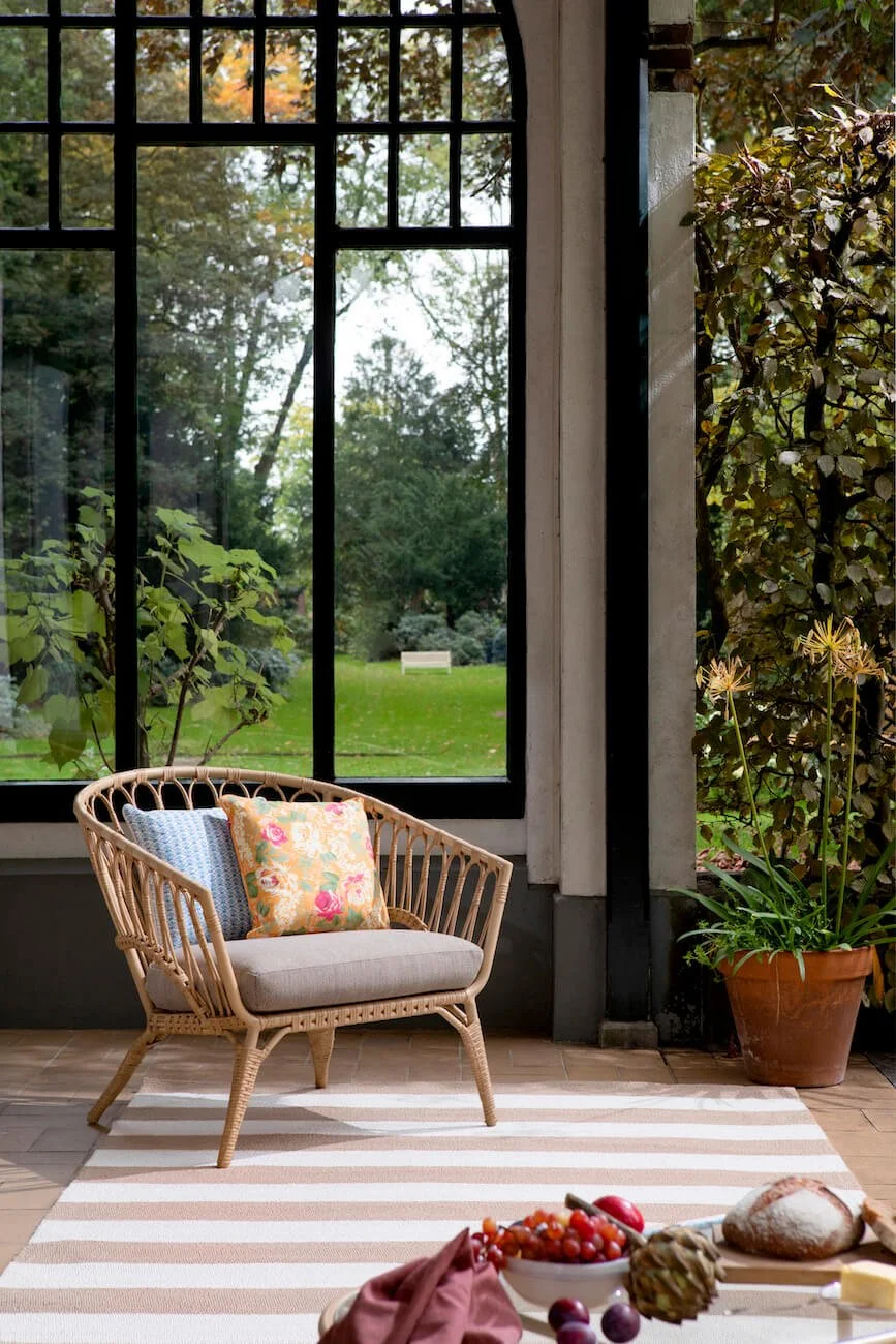 a stripy rug with a wicker chair and floral cushion with black framed large windows behind