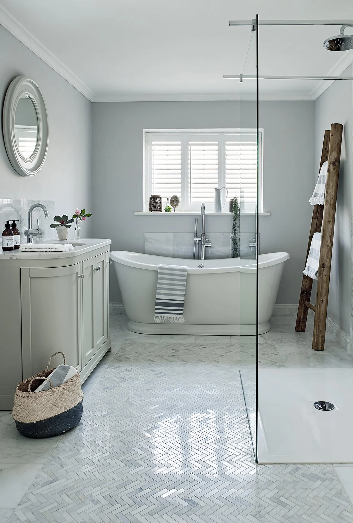 A bathroom with a roll top freestanding bath a ladder for towels against the wall and a curved vanity