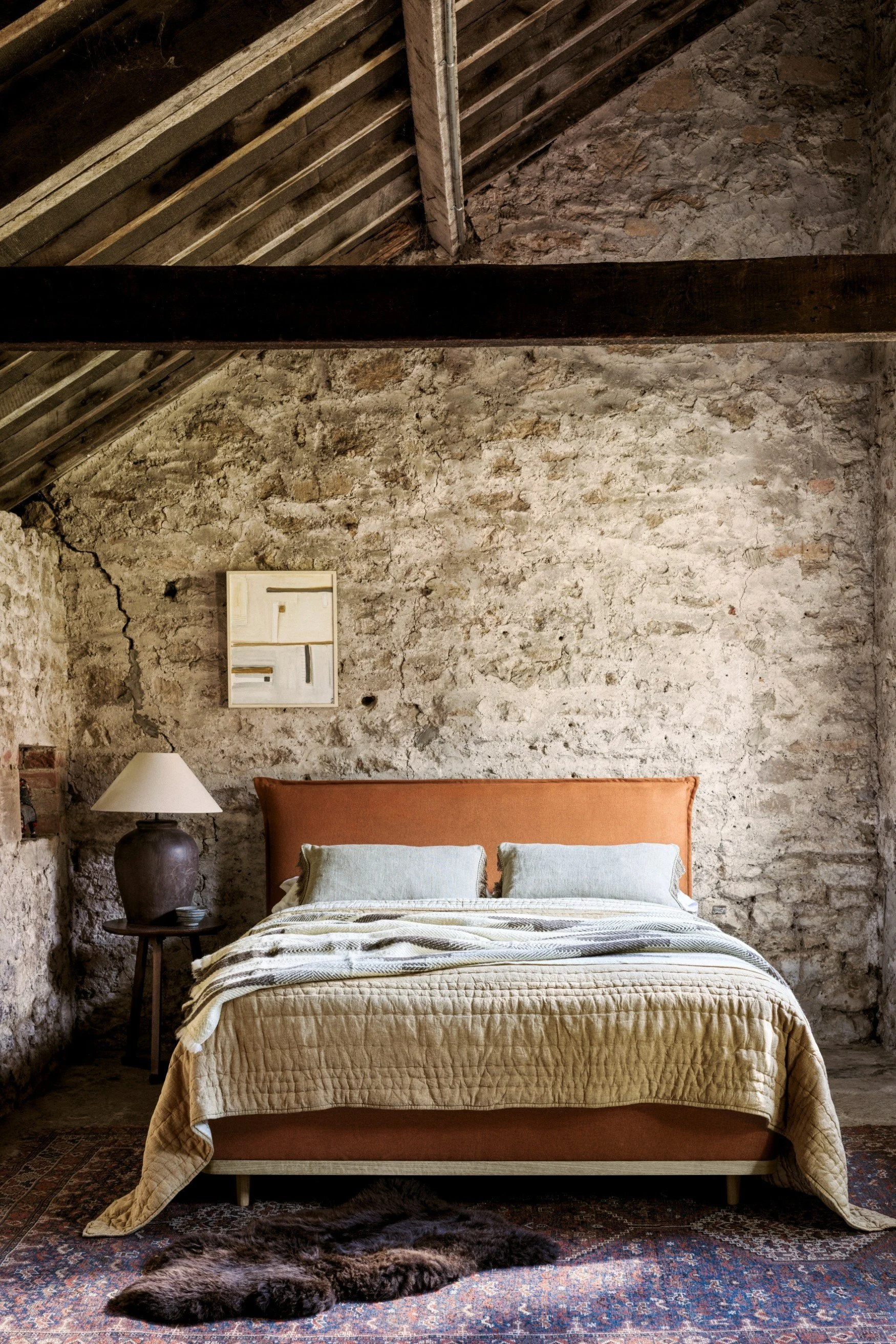 A bed in burnt orange against a rough stone wall