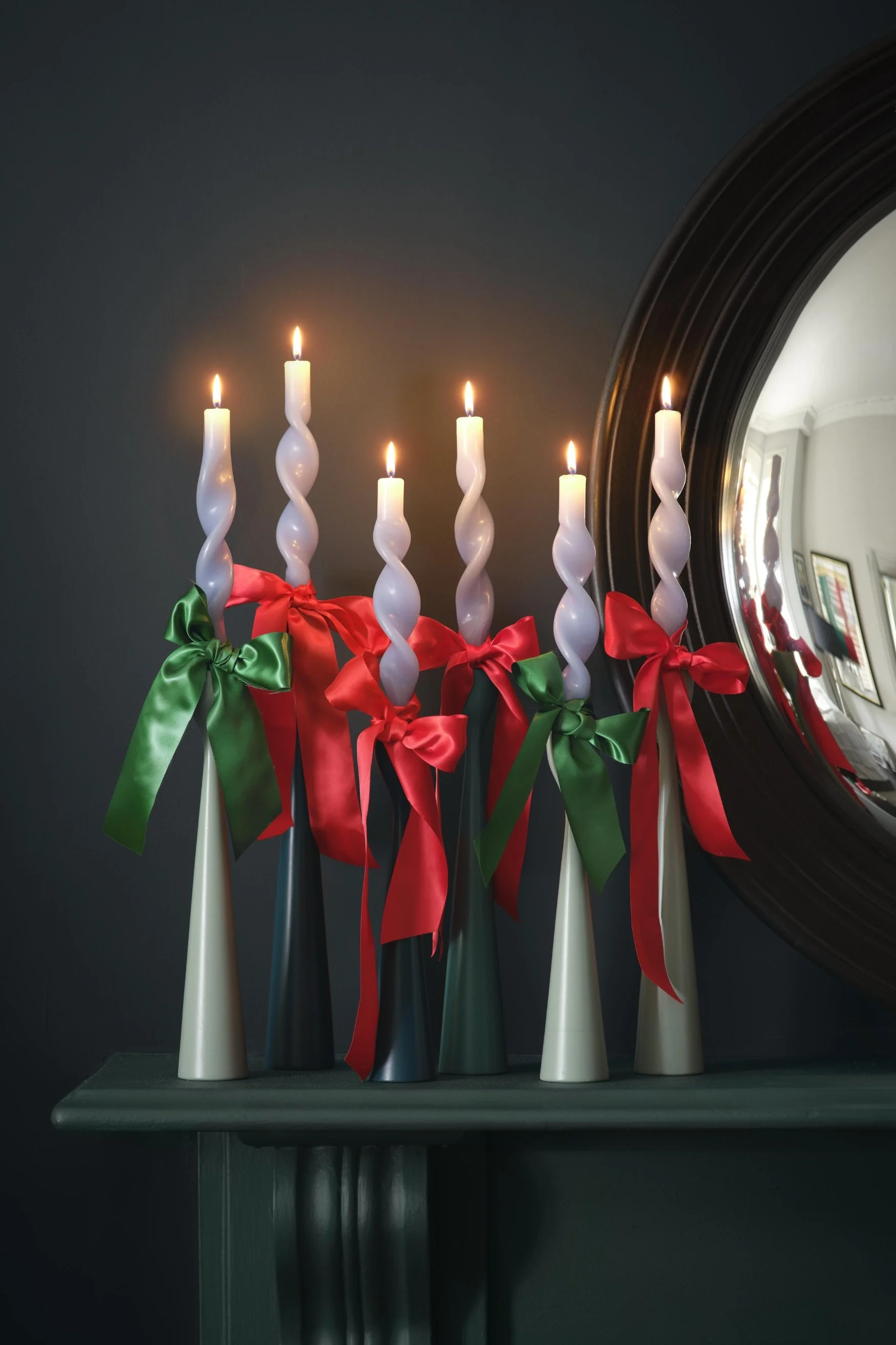 Five candle holders in a cone shape with twisted white candles  and ribbons in red and green tied in bows