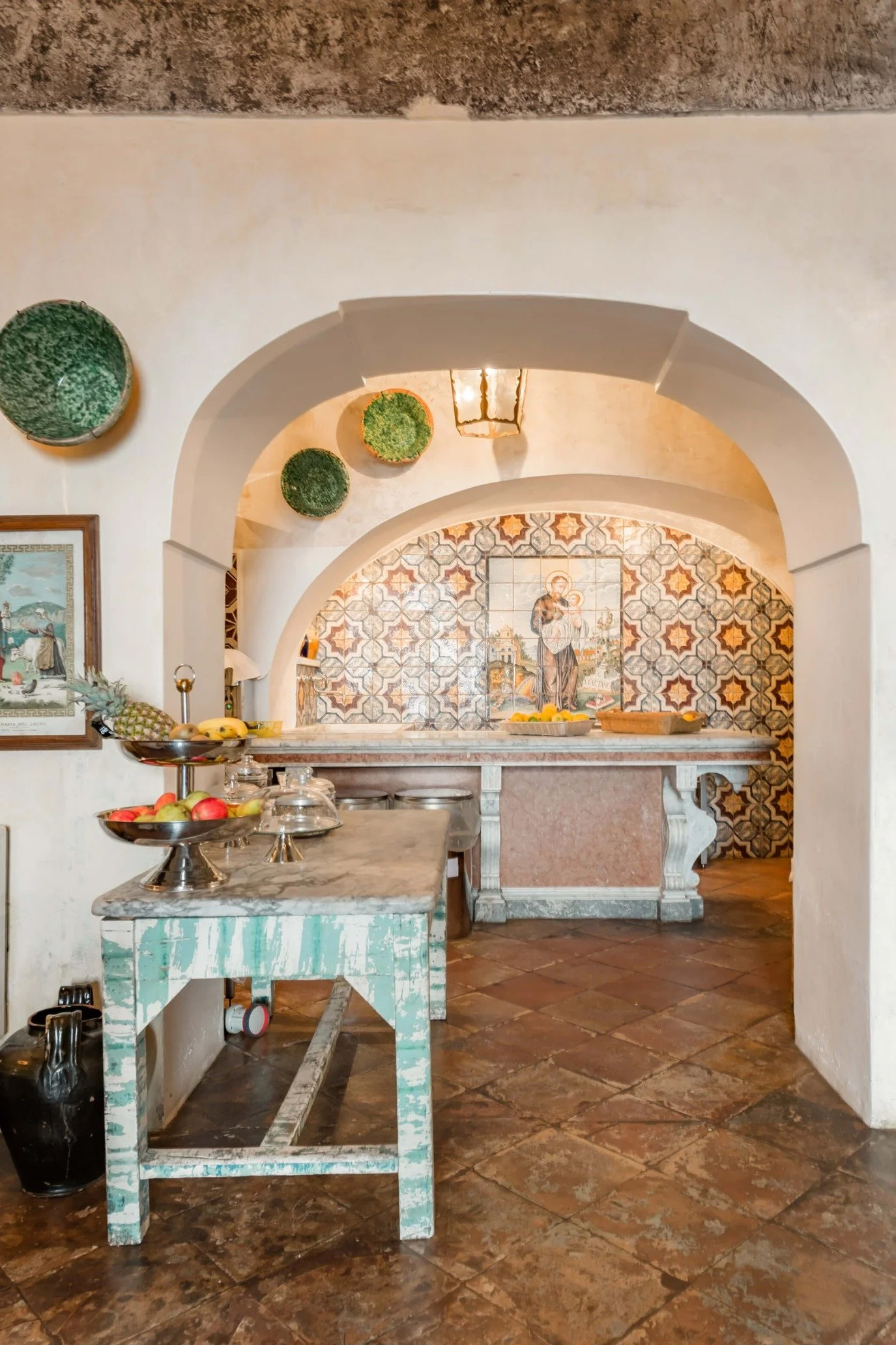 Luxury Mediterranean villa kitchen with traditional pizza oven, terracotta flooring and patterned Italian wall tiles.