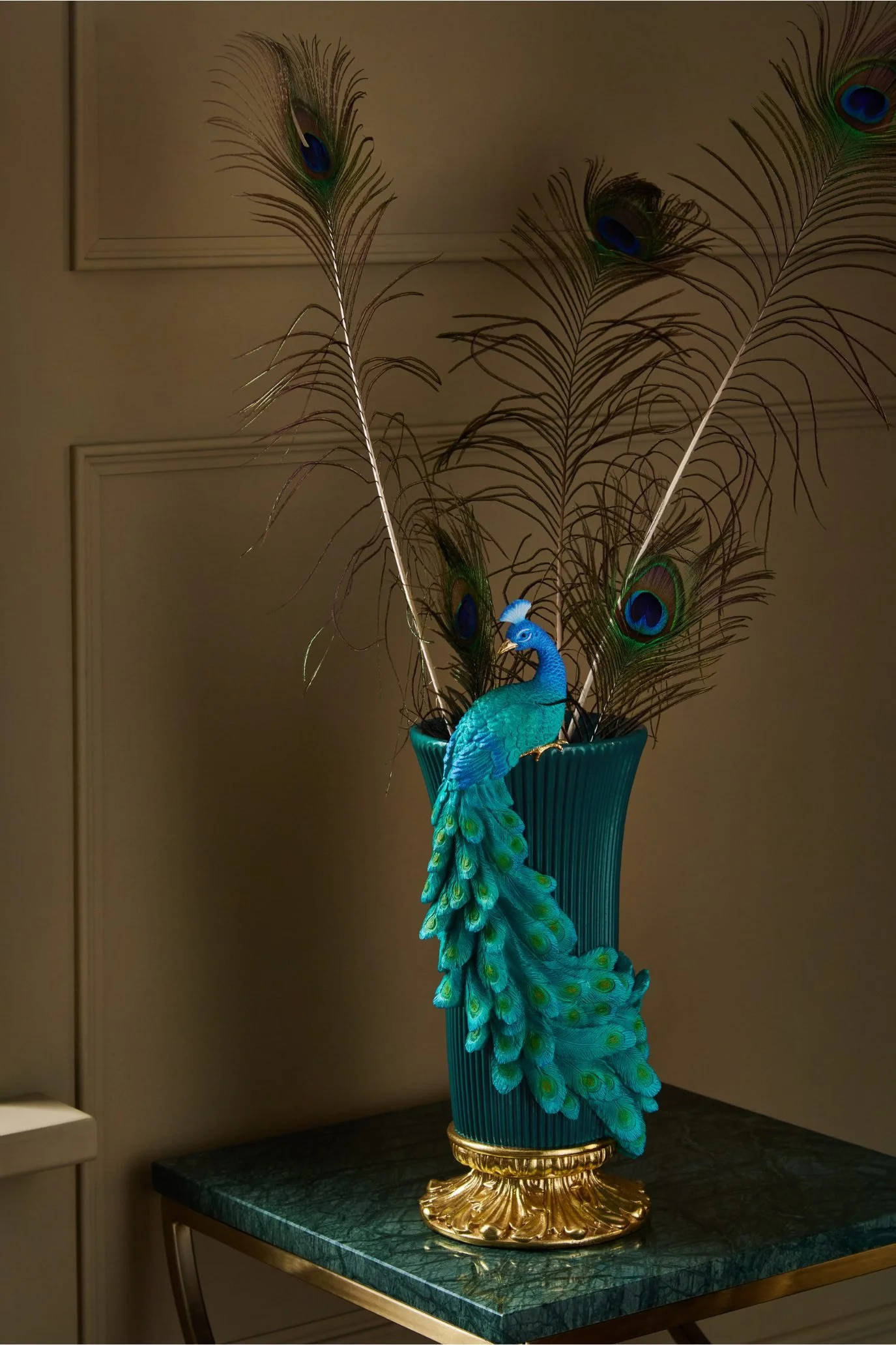 Blue fluted vase with gold accents, a sculpted peacock and tall peacock feathers.