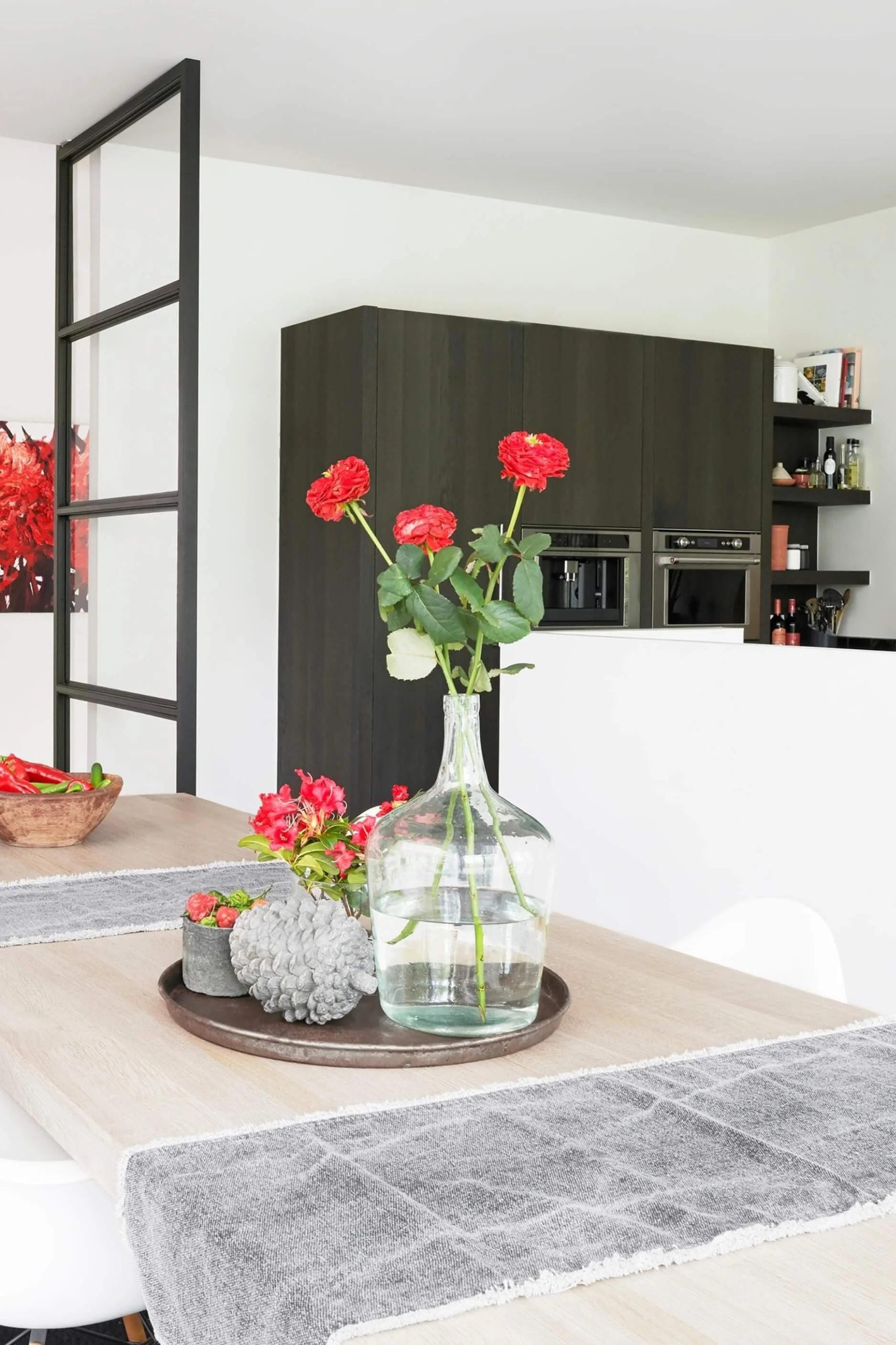 A dining area with a metal tray displaying a vase with red flowers and dishes with red chilli peppers  with black-framed doors and dark wooden cabinetry