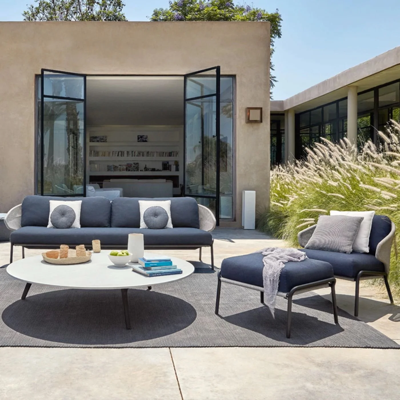A contemporary outdoor sofa and chair set in blue and white next to a large white coffee table