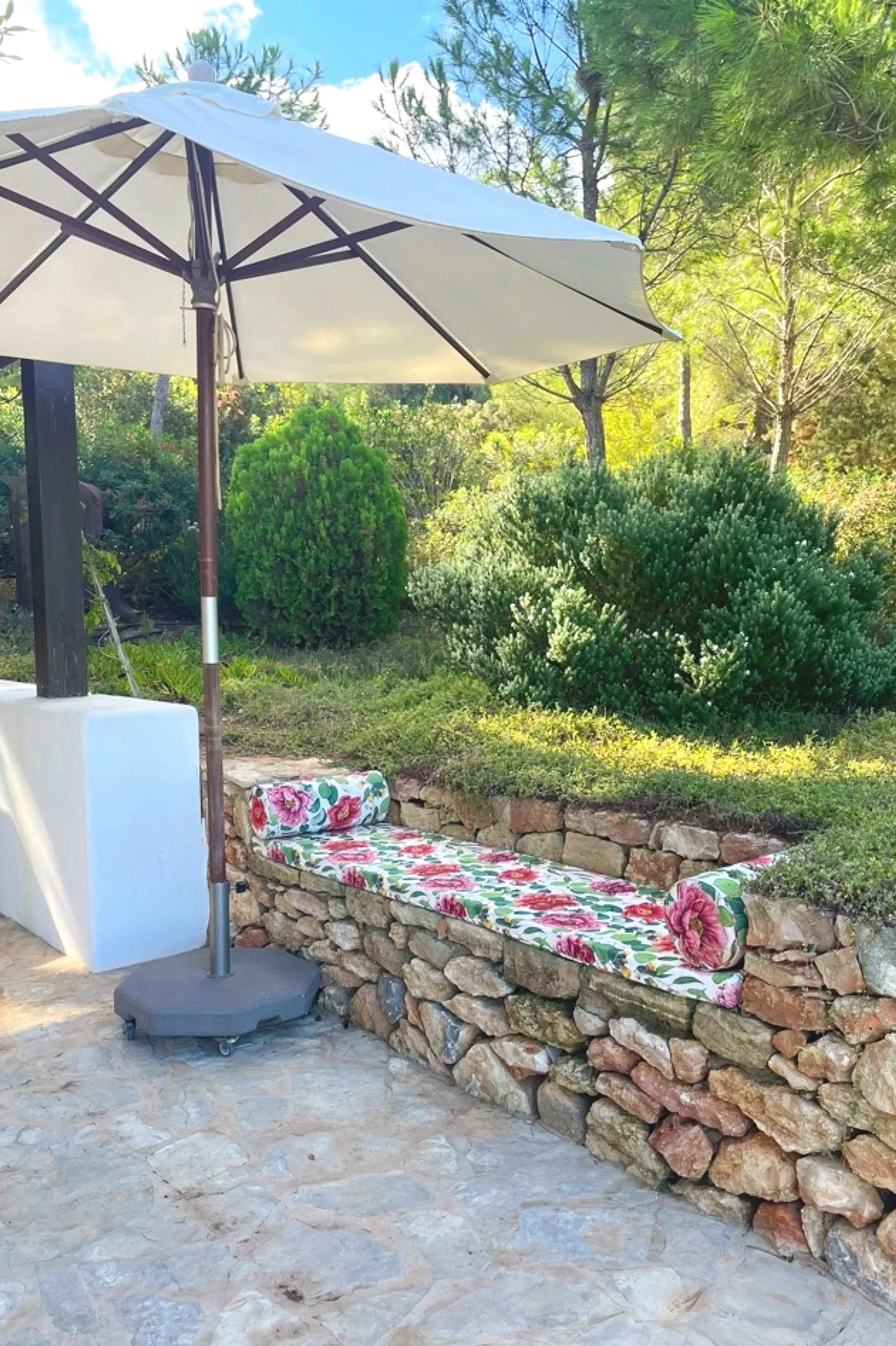 Outdoor built-in bench with floral cushions beside a parasol in a garden