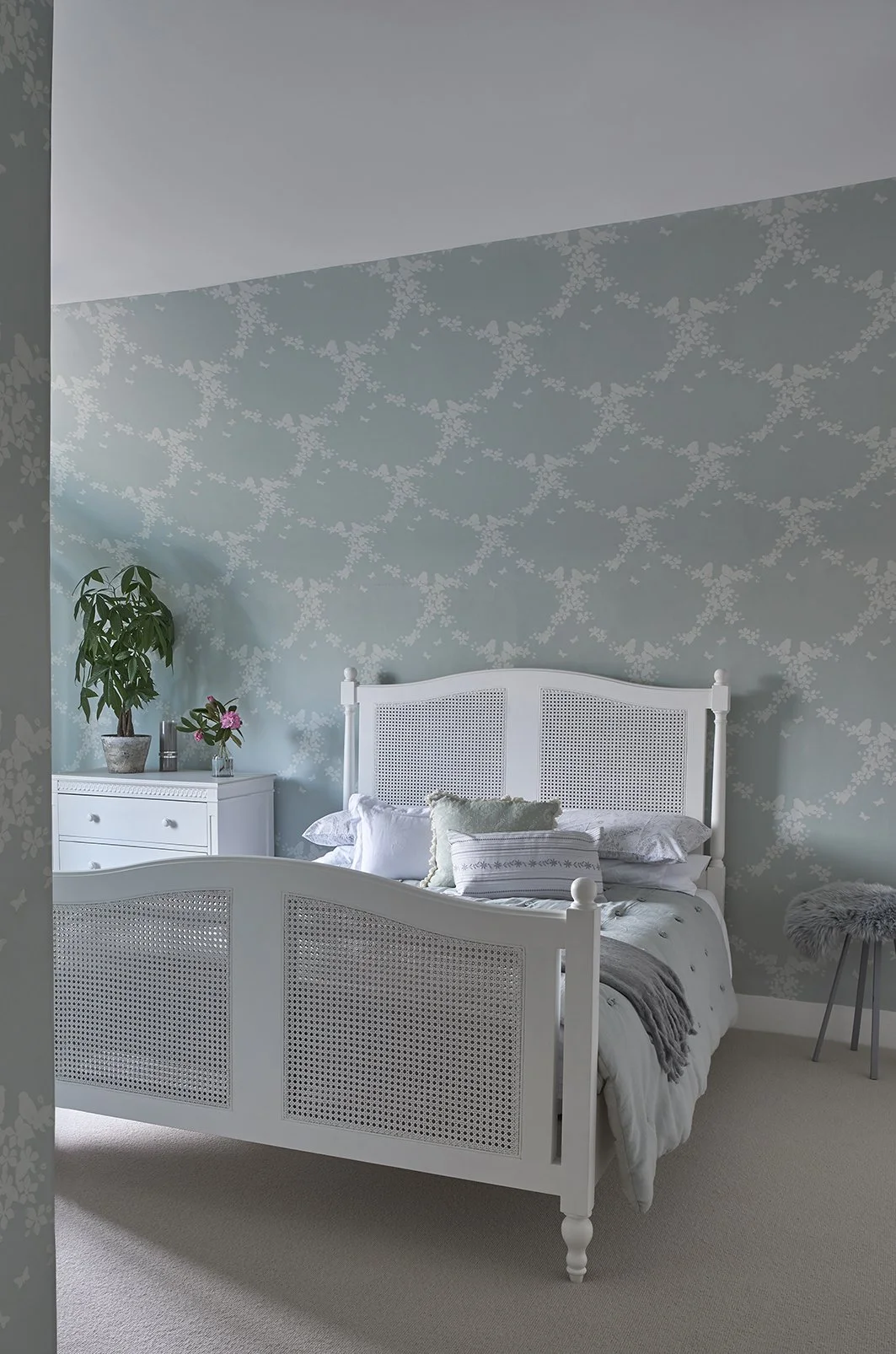 A white can bed frame dressed in white and green linen against a mint green wall