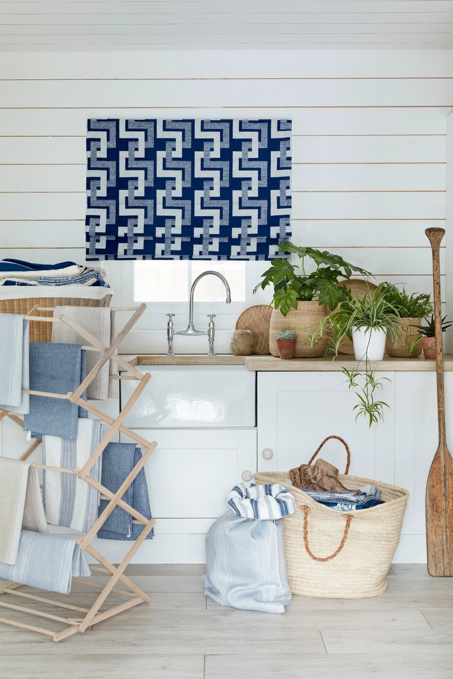 A blue geometric blind in a kitchen with plants on the worktop and a washstand with more blue fabric