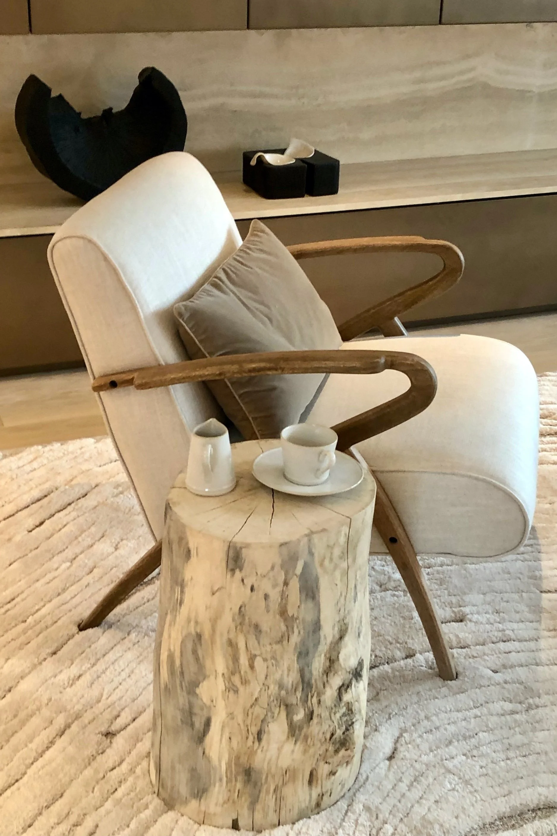 A cream and wood chair with a tree trunk table next to it with a cup, saucer and jug on top of it