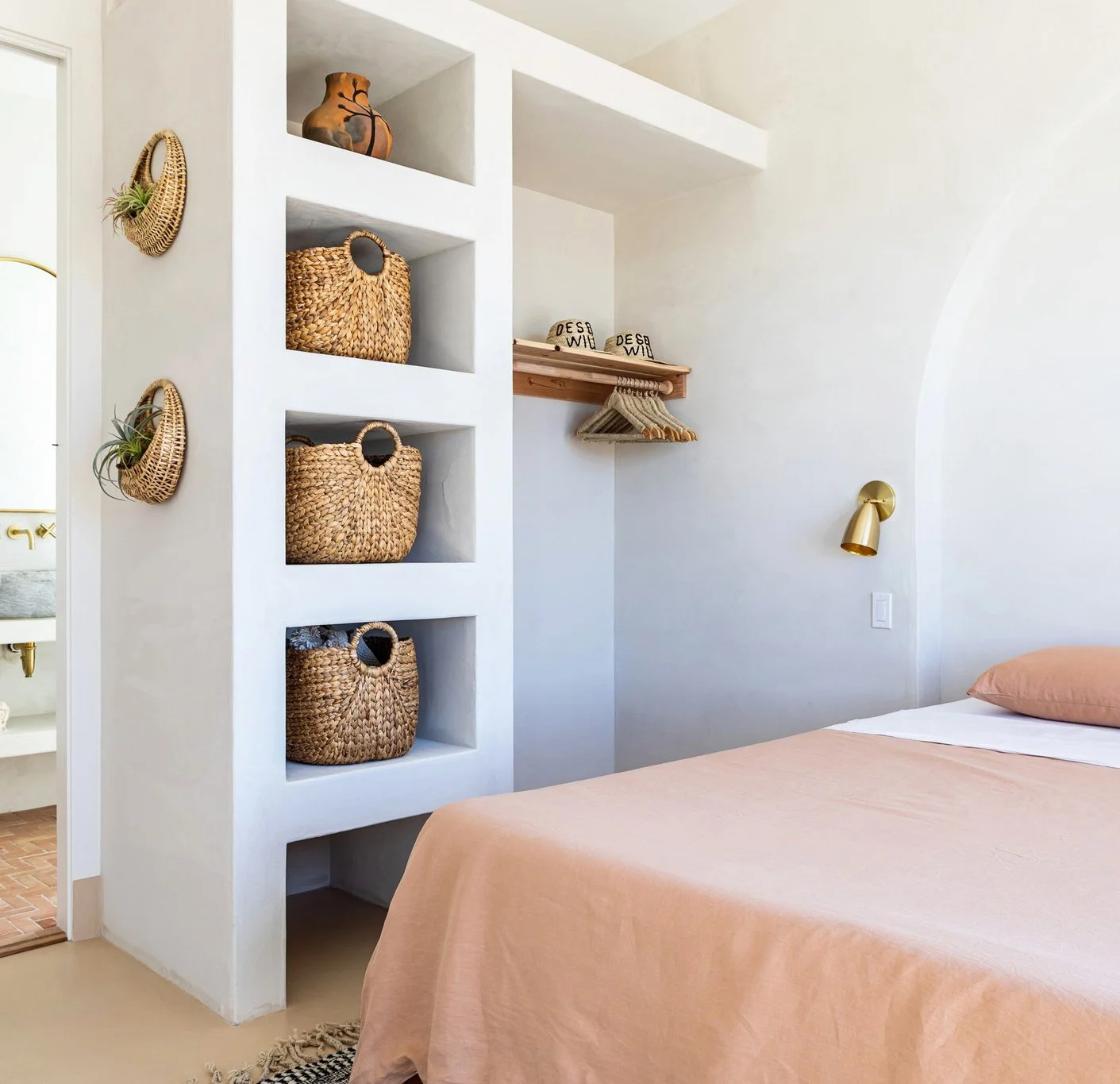 large plaster arch behind the bed, which creates a striking headboard. There are also woven storage baskets, brass wall sconces, and even Desert Wild custom-made sun hats.