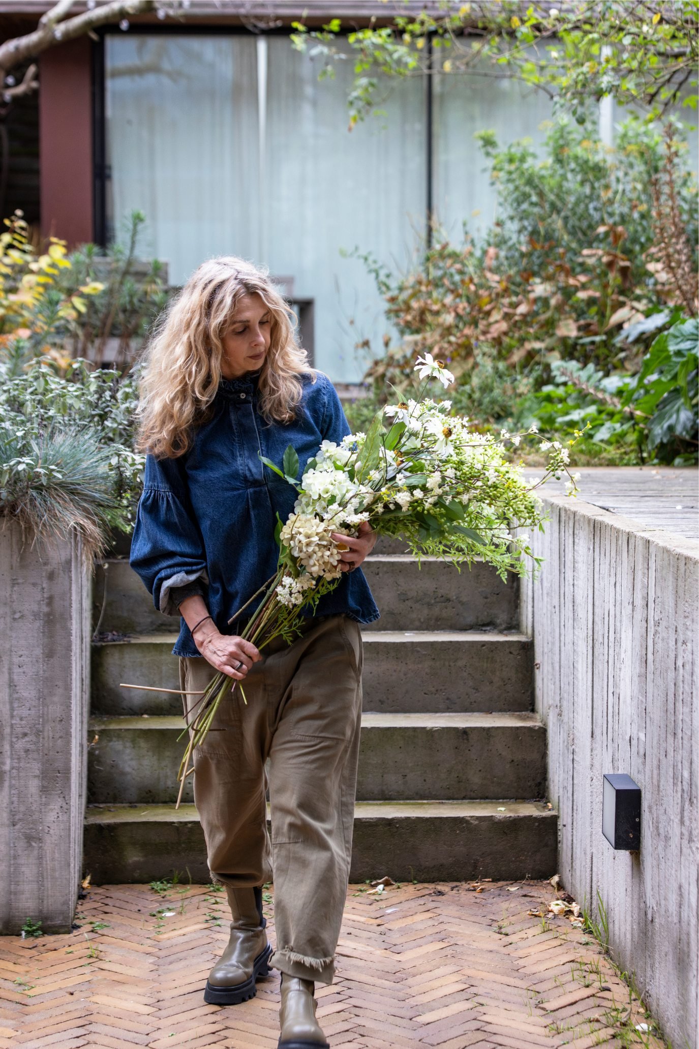 Woman carrying a large natural-looking bouquet of white faux flowers and foliage outdoors.
