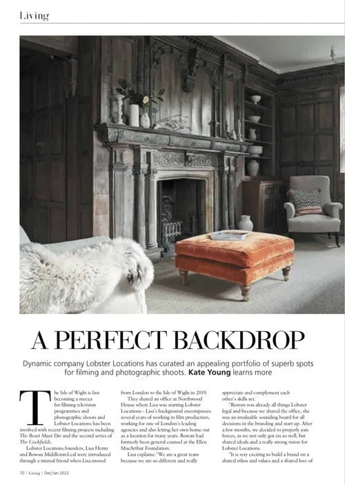 Magazine tear sheet of a heritage living room with dark wood paneling, a marble fireplace, and plush furniture, including a white fur-covered chair and a burnt orange ottoman.
