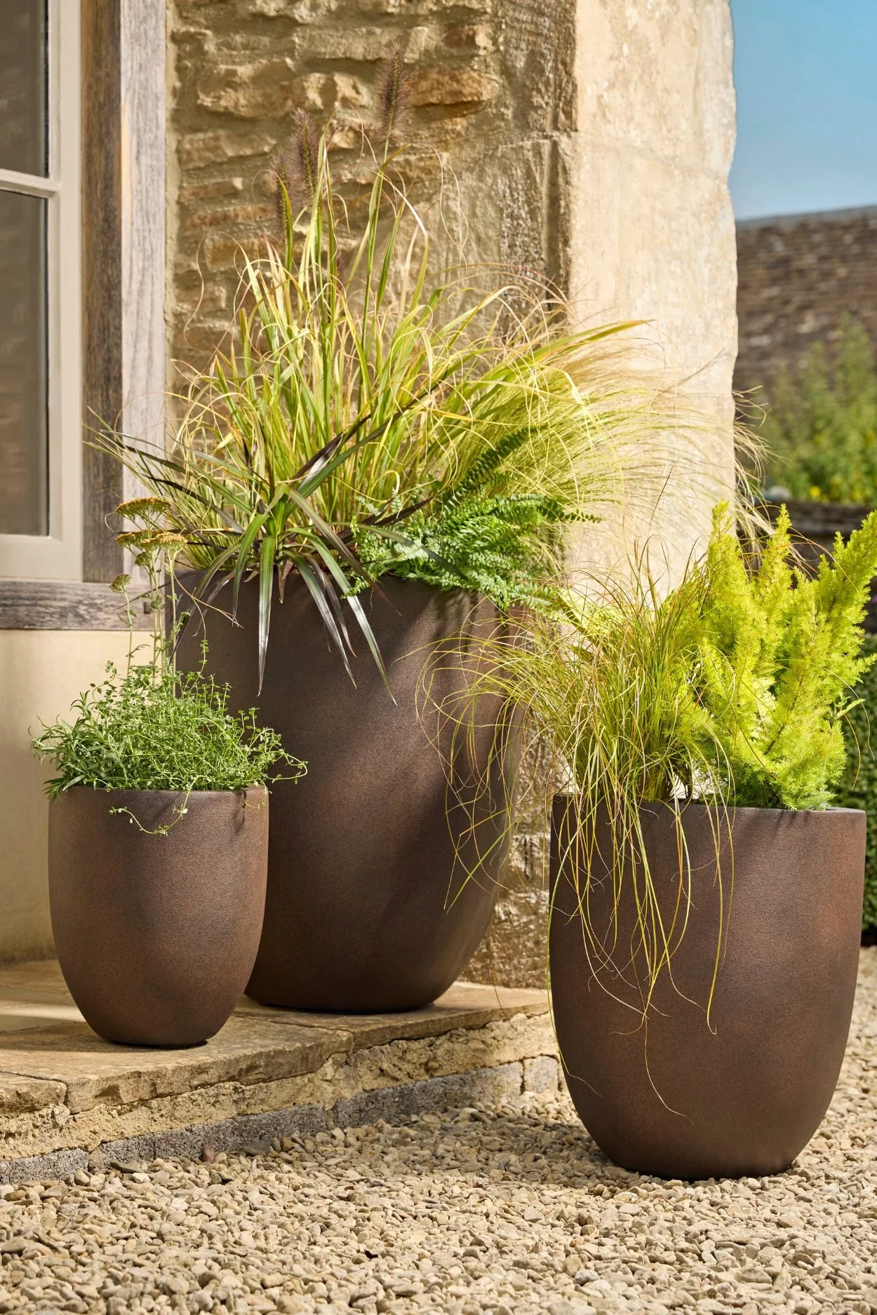 Three aged rust-effect planters by Cox & Cox filled with ferns and grasses