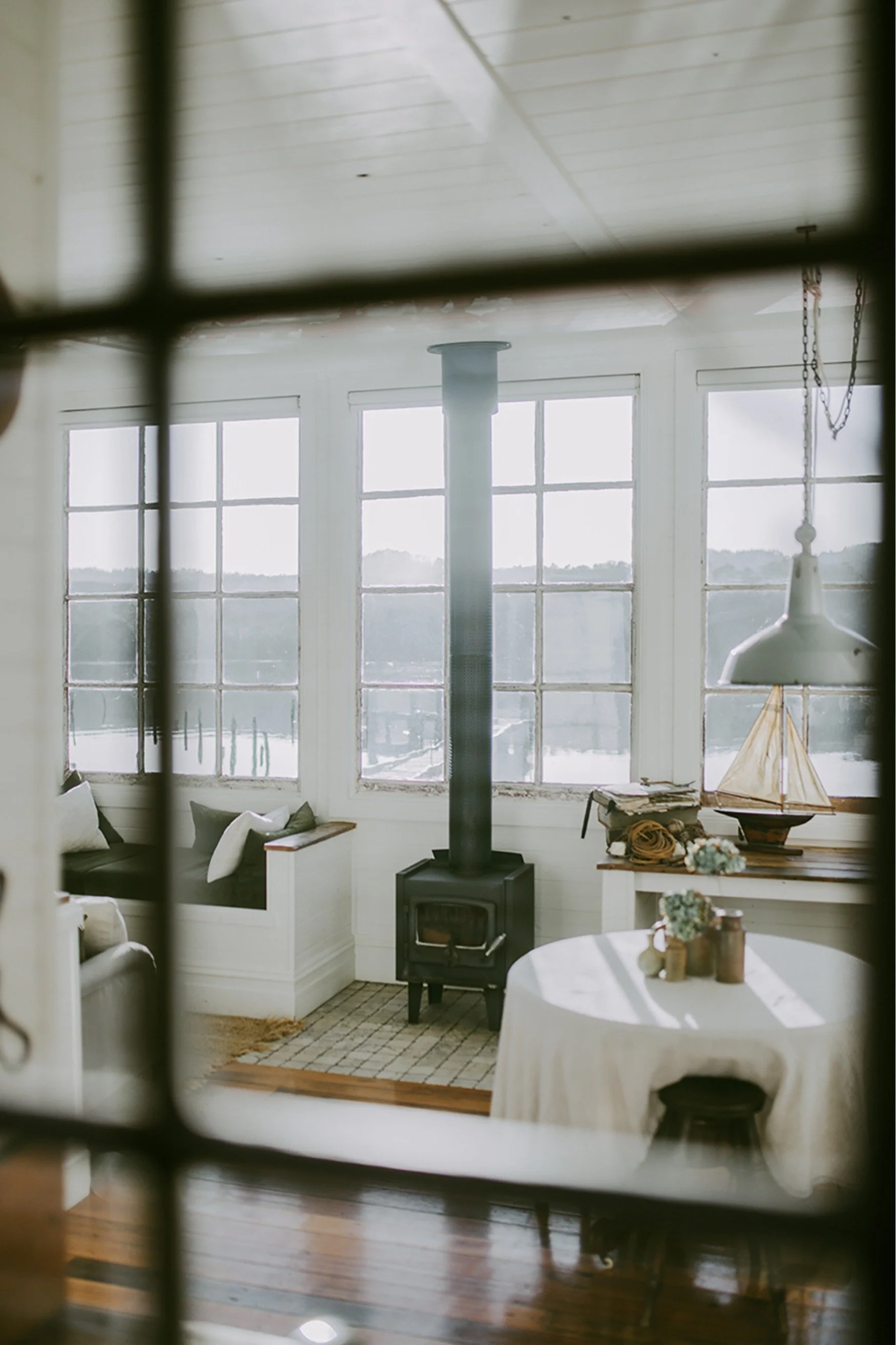 View through a window to a wood burner and day bed and windows overlooking the sea