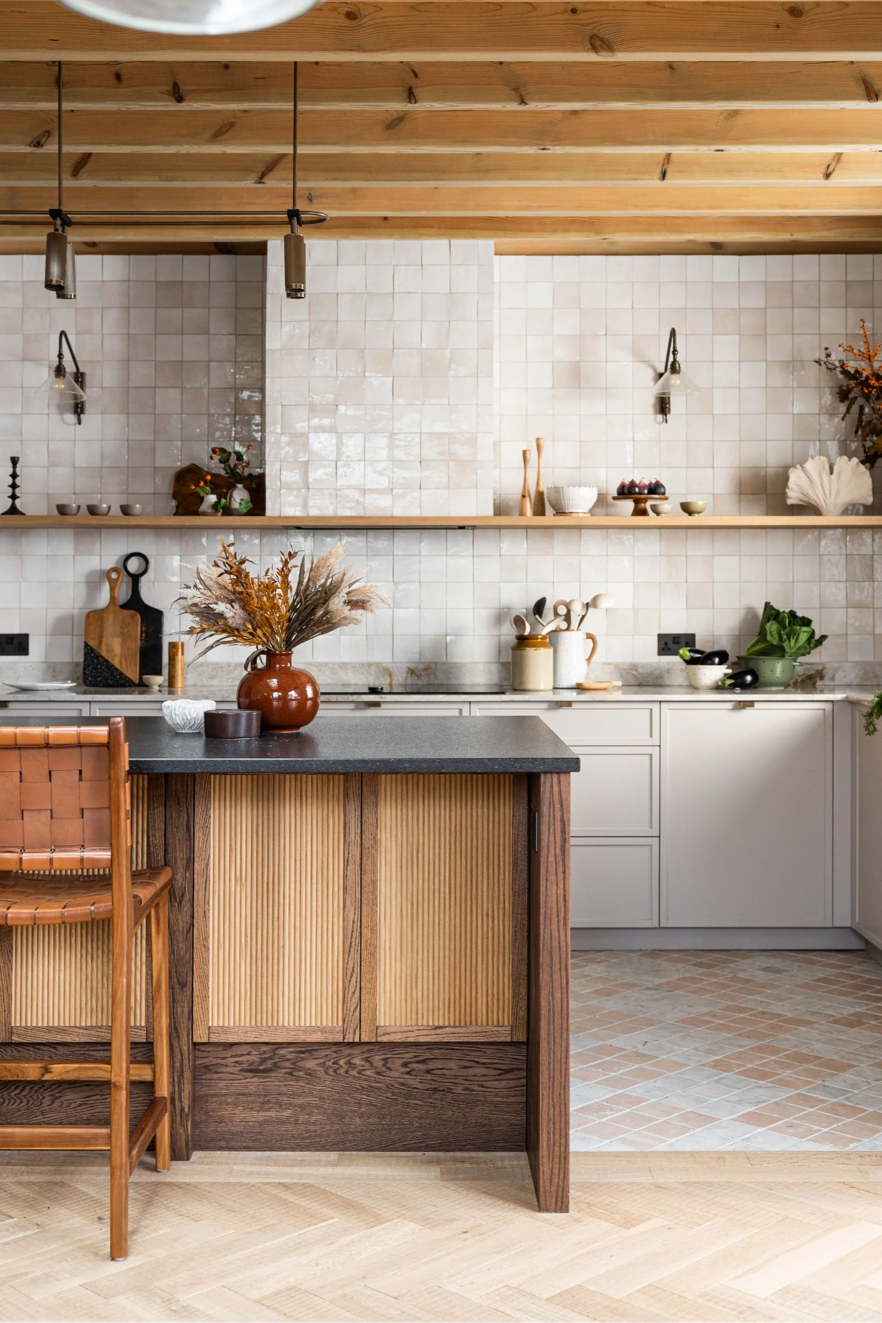 A kitchen with square pearl-toned tiles an exposed wooden beamed ceiling and wood fluted cabinets