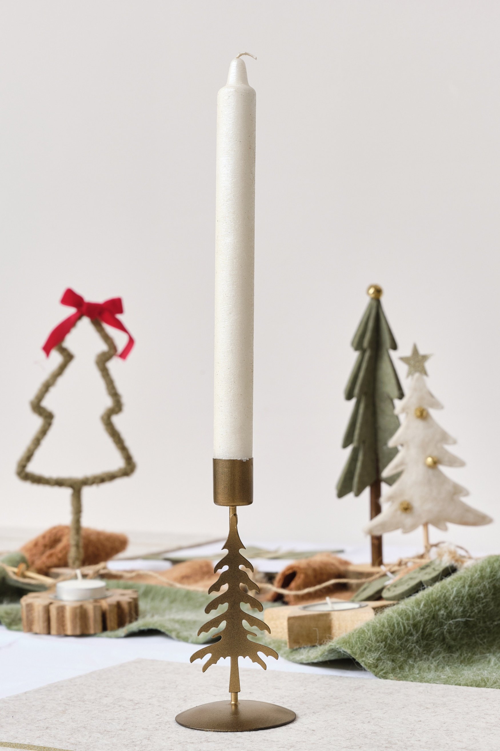 A christmas tree shaped bronze candle with a white candle stick infront of three little christmas tree decorations