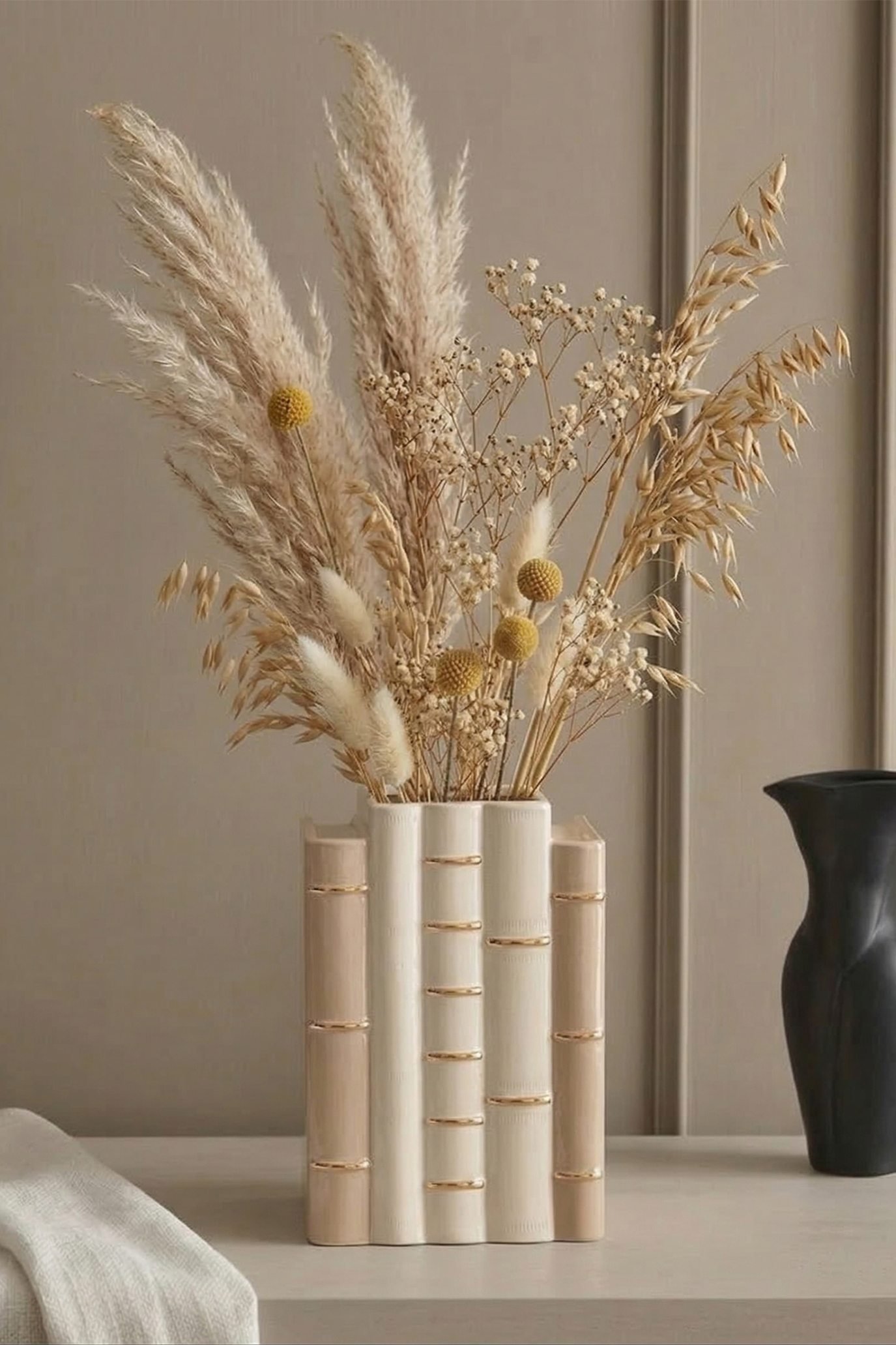 Ceramic vase shaped like stacked vintage books filled with dried grasses and flowers.