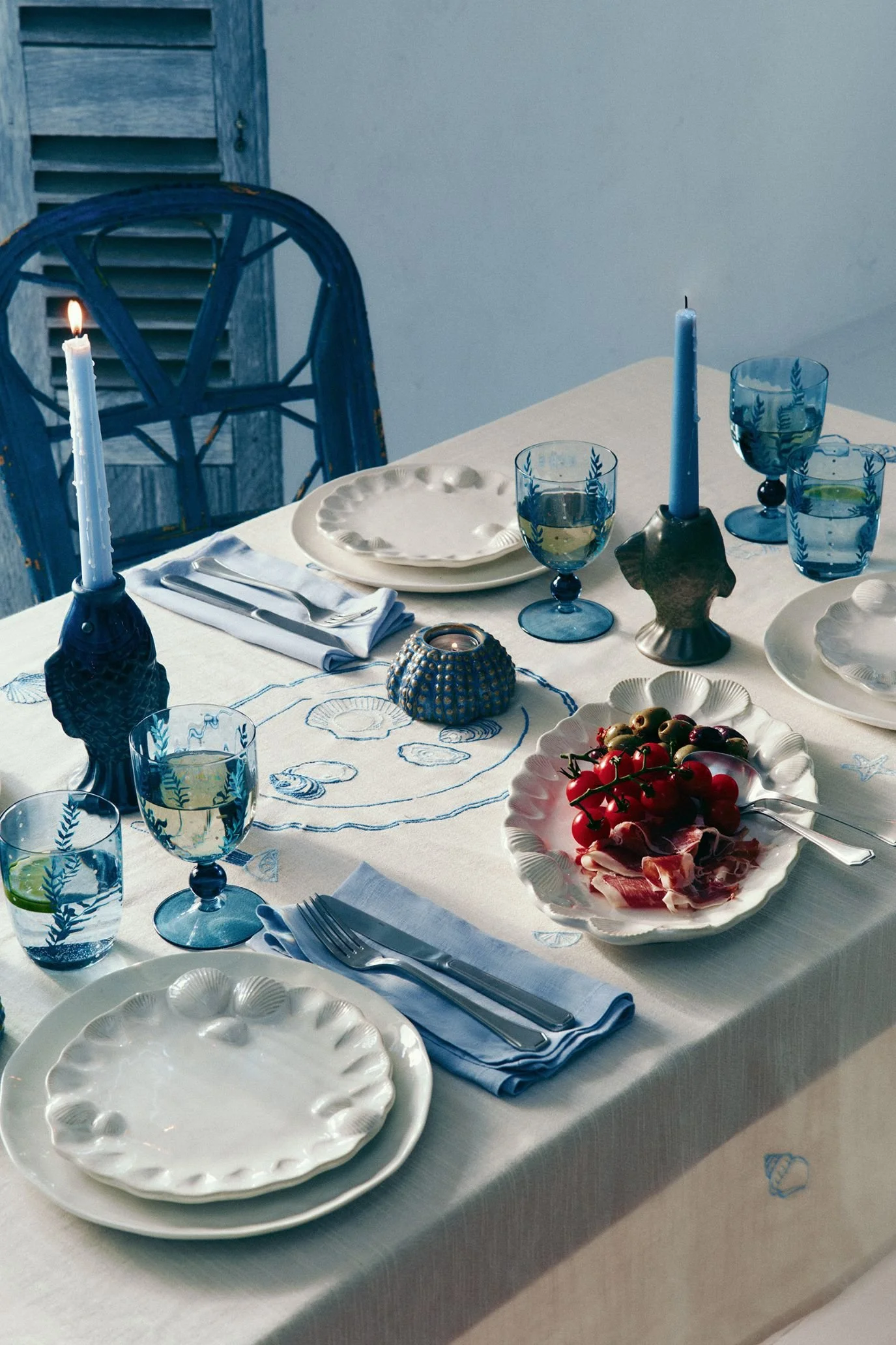 Coastal stoneware plates with raised shell detailing styled with blue napkins and glassware.