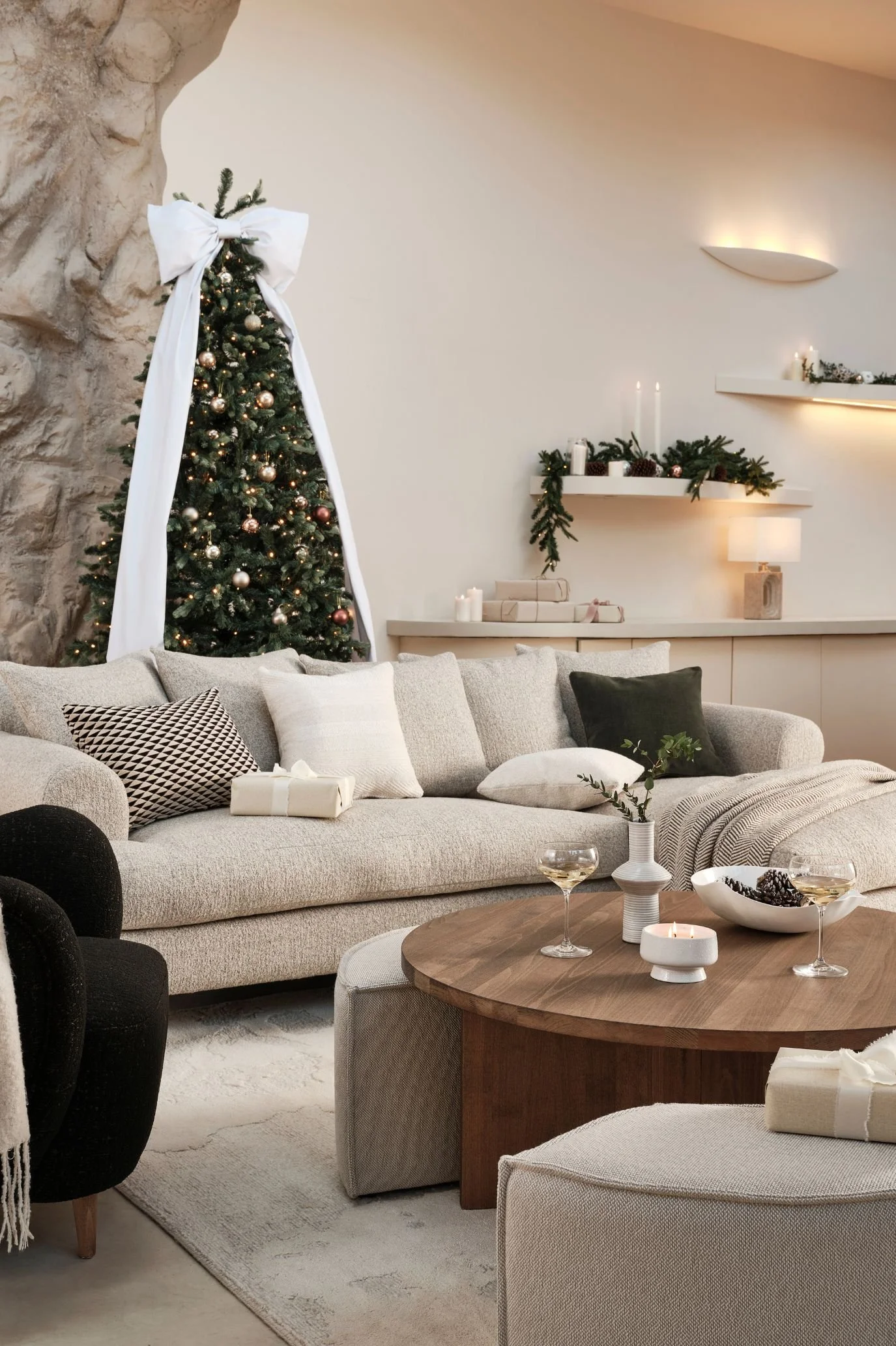 Christmas tree topped with an oversized white bow with long trailing ribbons in a neutral living room.