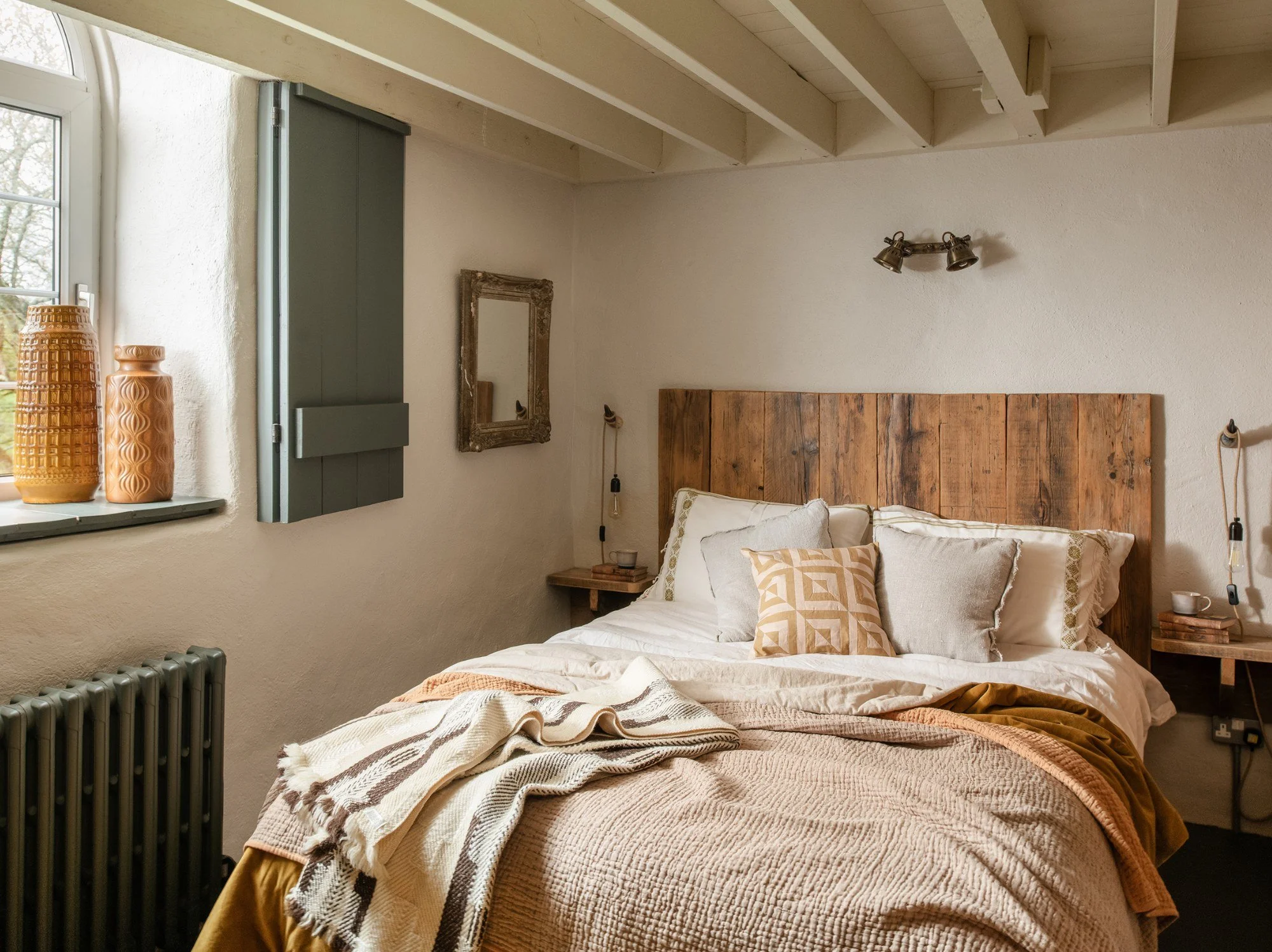 Cosy rustic bedroom with stone walls, layered bedding, lambswool blankets and handcrafted wooden furniture.