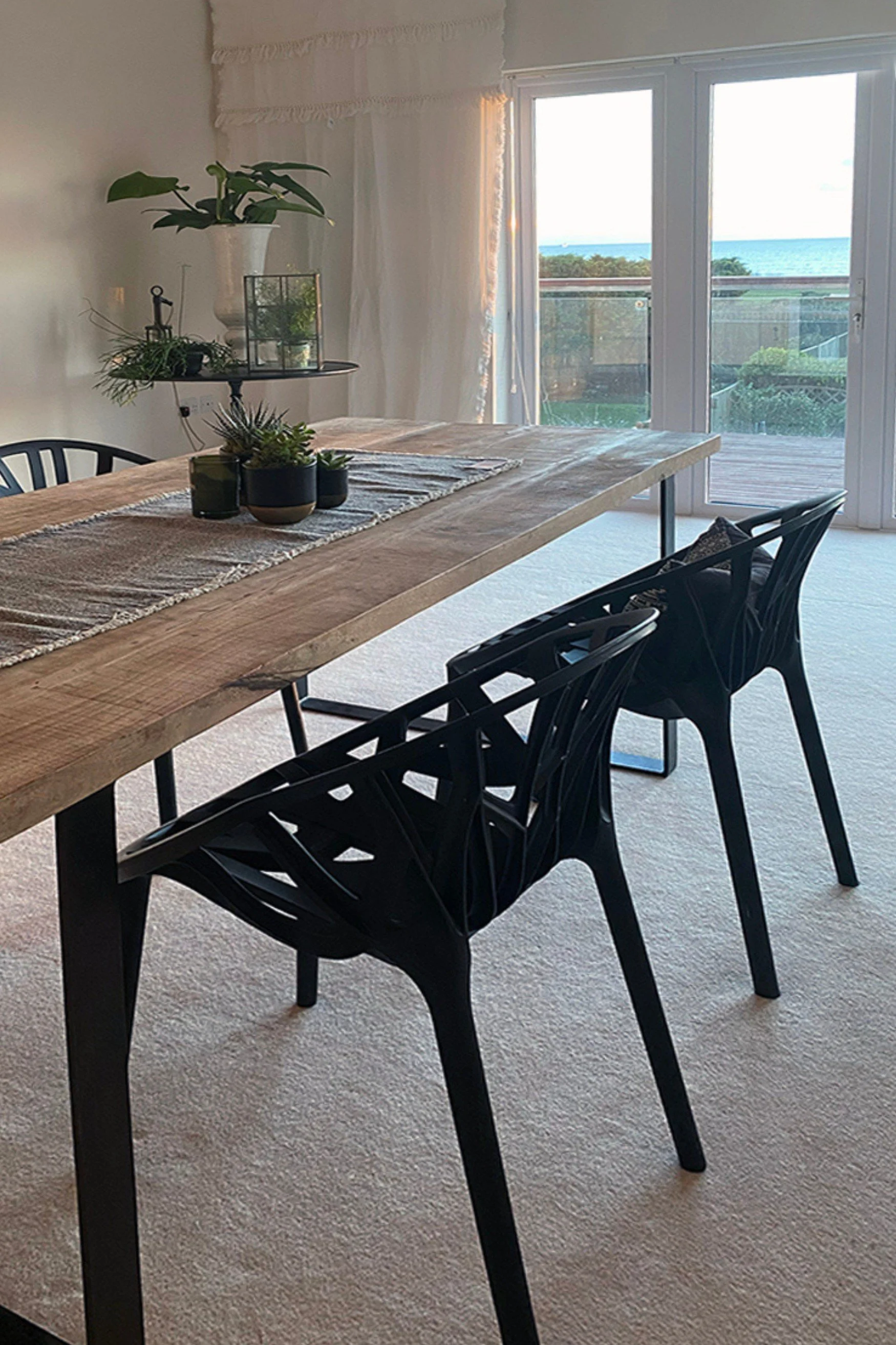 Dining room with wood table and black chairs with a view from white French doors and plants dotted around