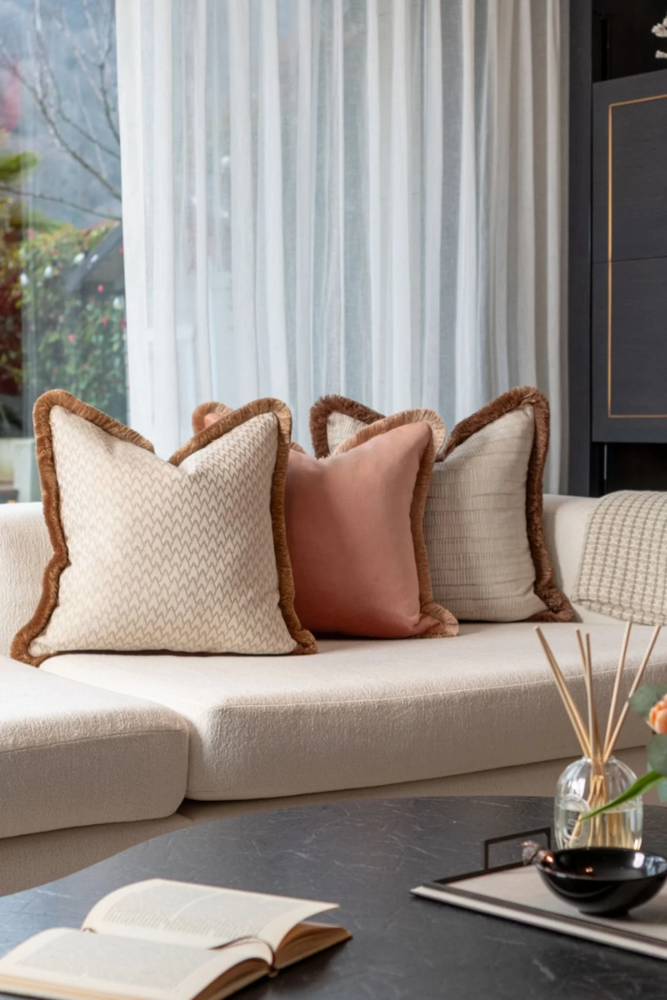 Neutral and terracotta cushions with decorative trims arranged on a pale sofa